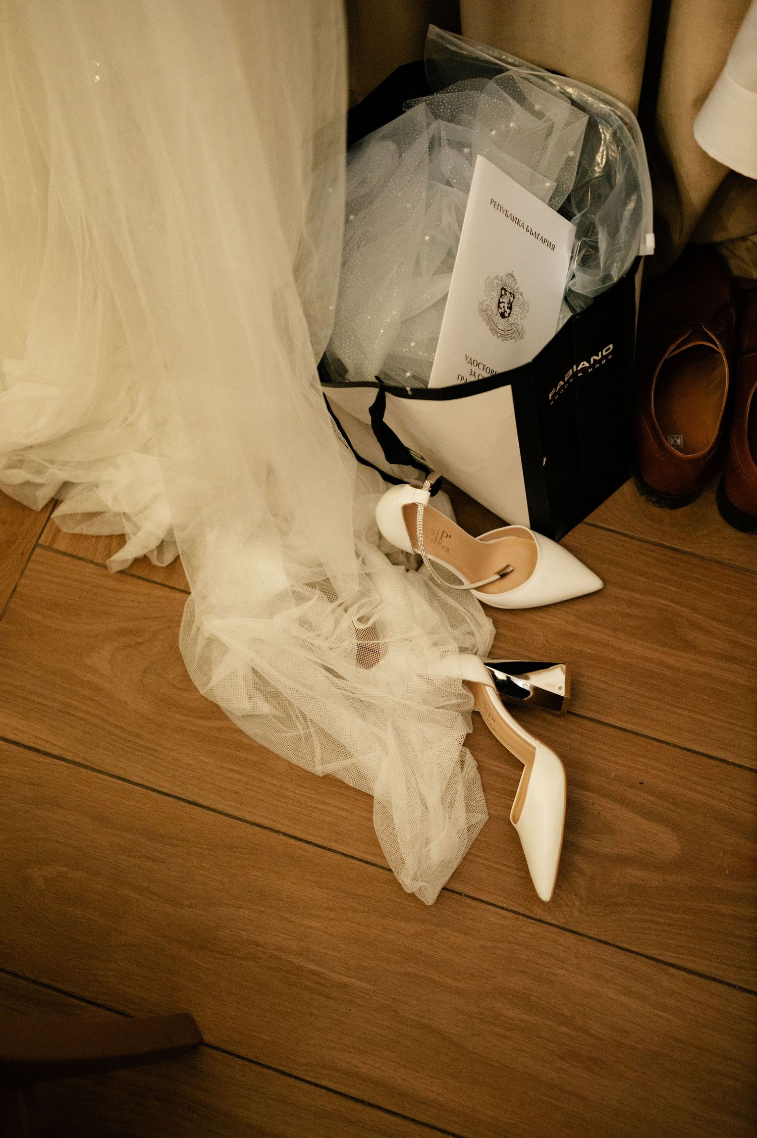 White bridal shoes and tulle veil arranged on hardwood floor with other wedding accessories.