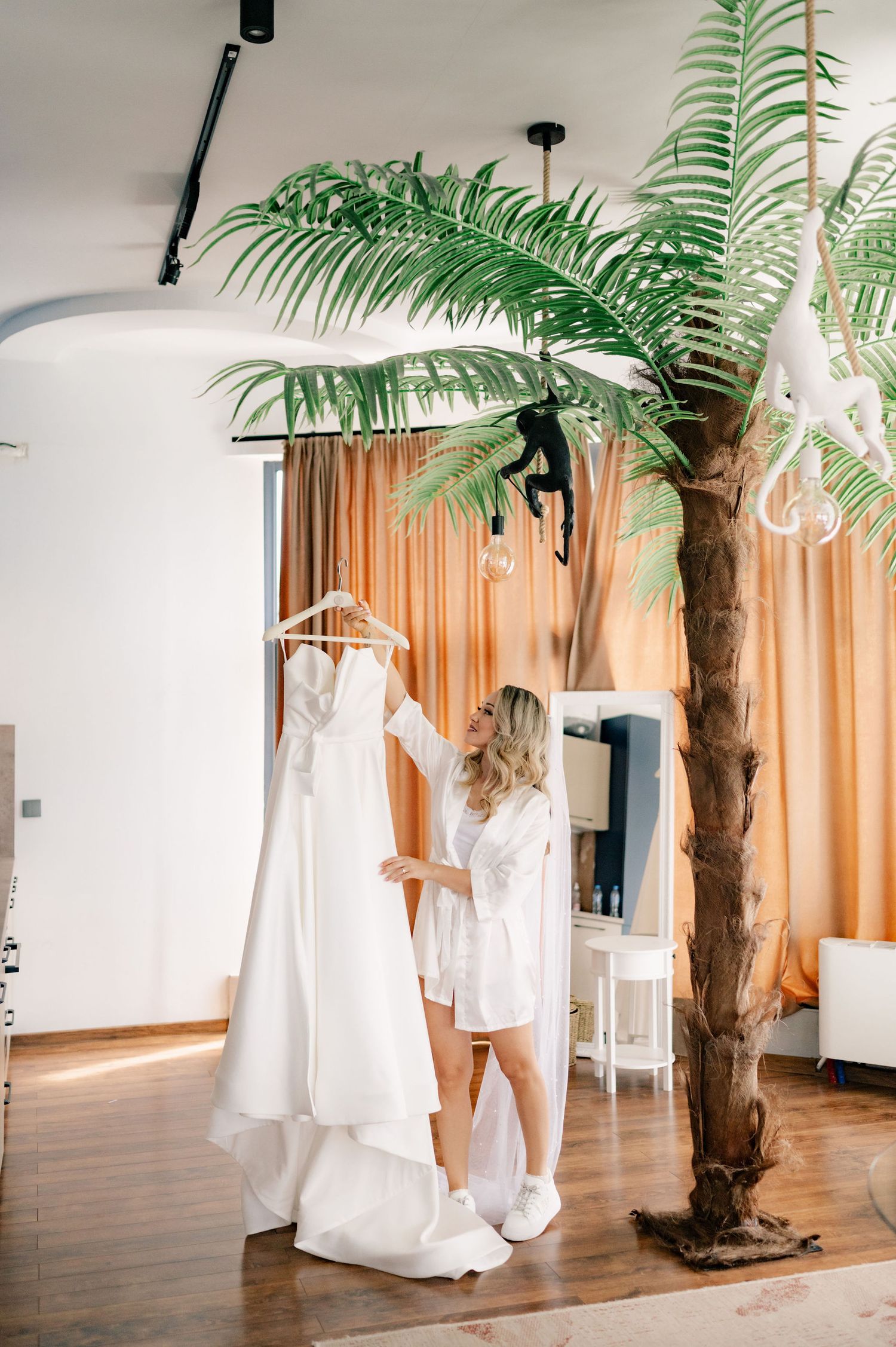 White wedding dresses hanging on display next to a decorative palm tree in a bridal boutique interior.