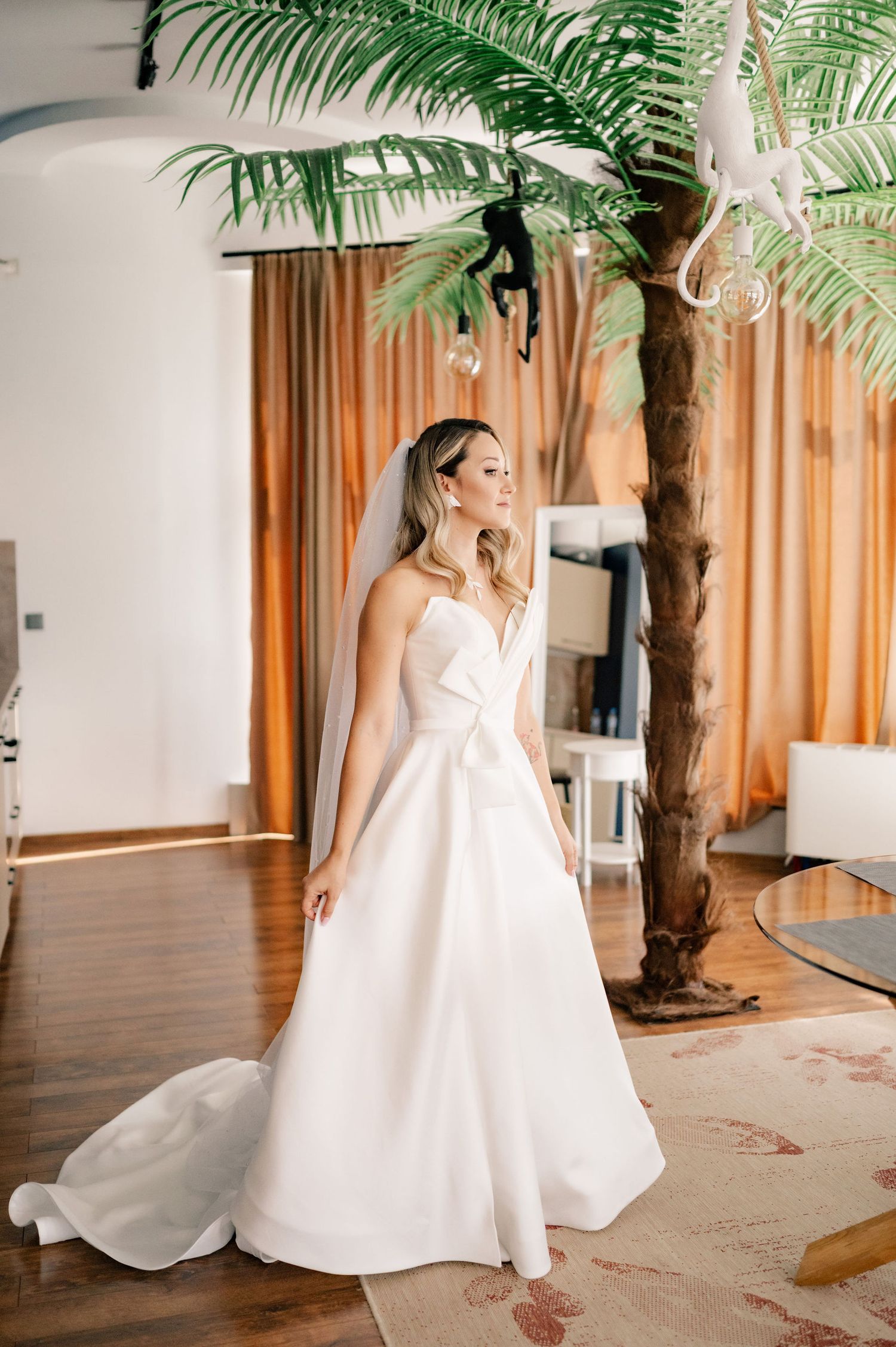 Elegant white wedding gown with a flowing skirt and fitted bodice photographed in an interior space with palm decor.