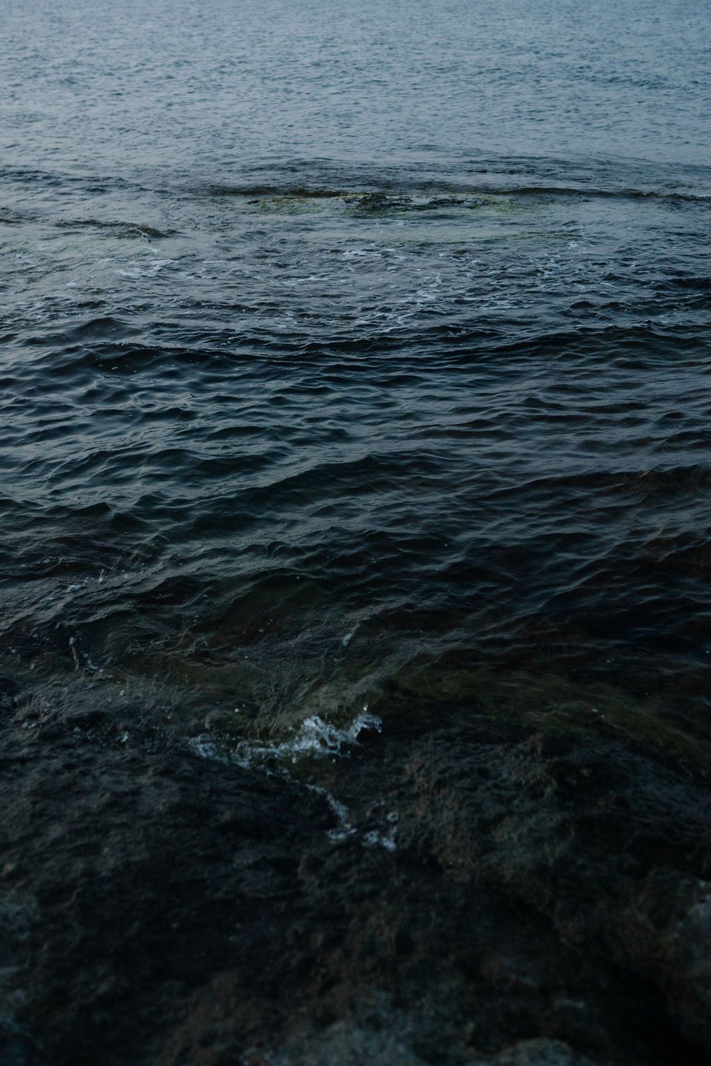 A sequence of dark ocean waves rippling across deep blue waters creating a moody seascape pattern.