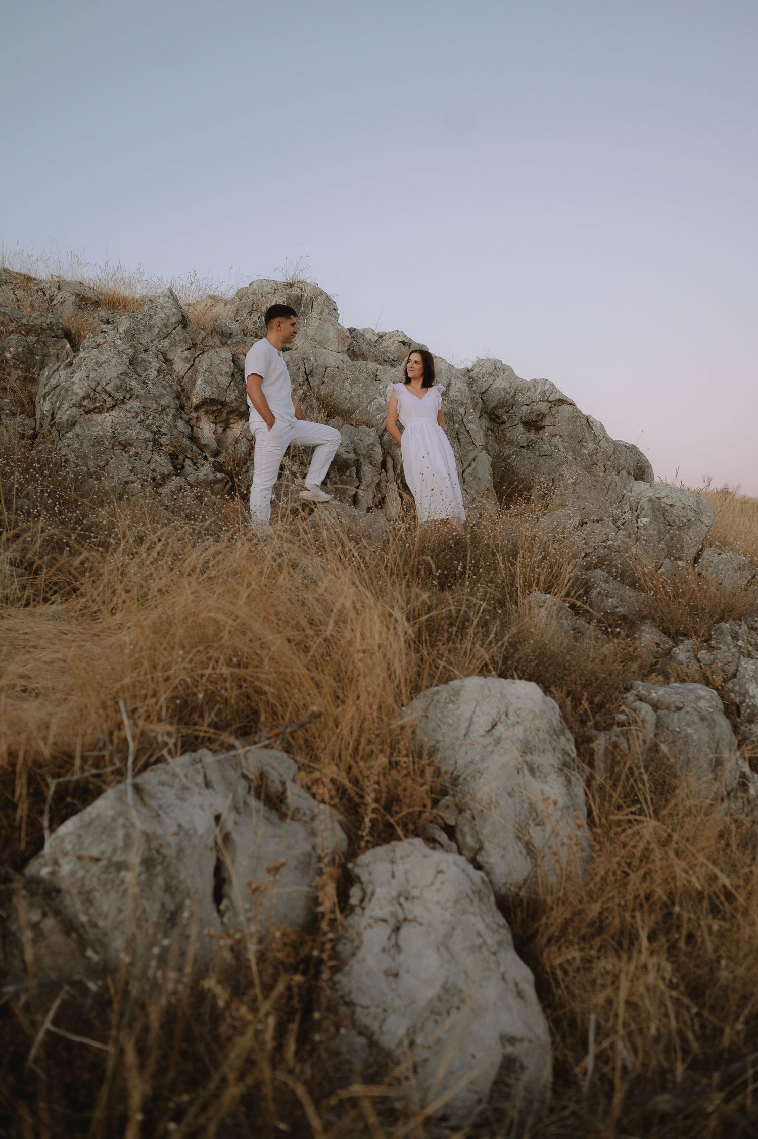 People in white outfits pose among dry brush and rocky terrain during golden hour.