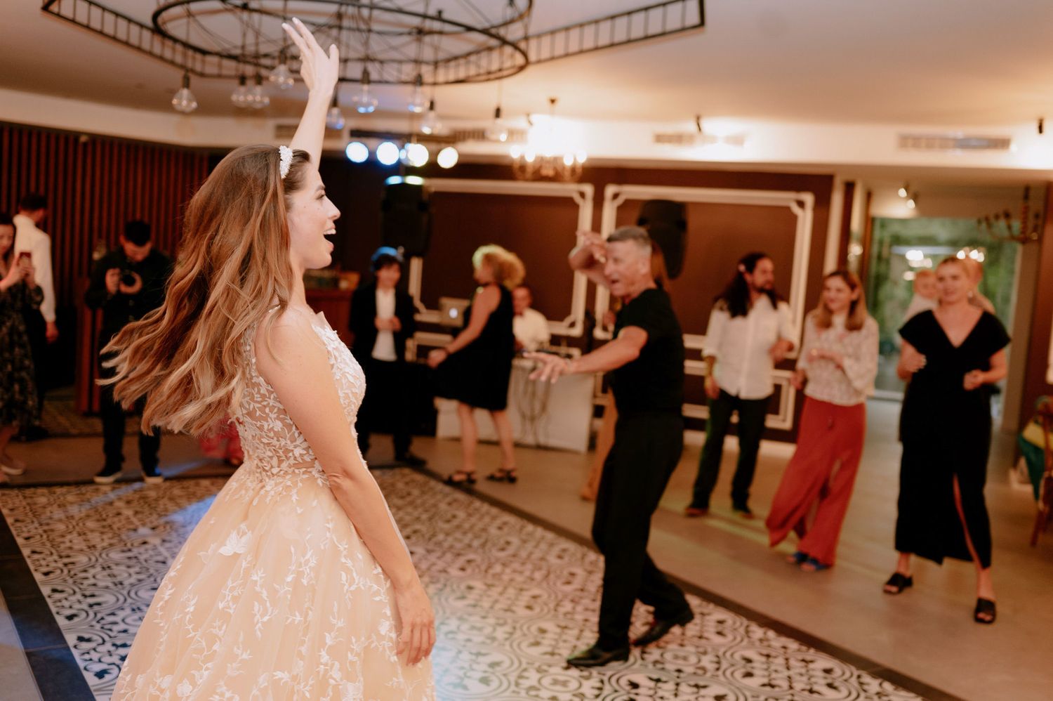 Couples dancing together at an elegant ballroom event with decorative lighting and patterned carpet floors.