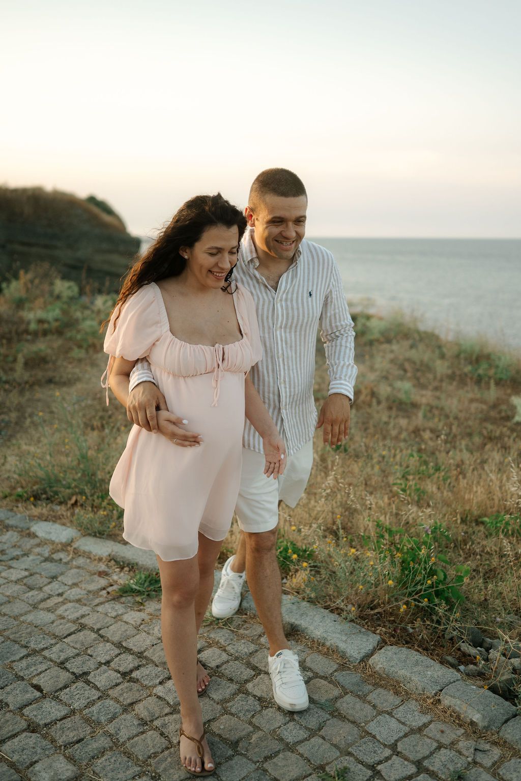 A couple shares a romantic moment walking together on a coastal path at sunset.