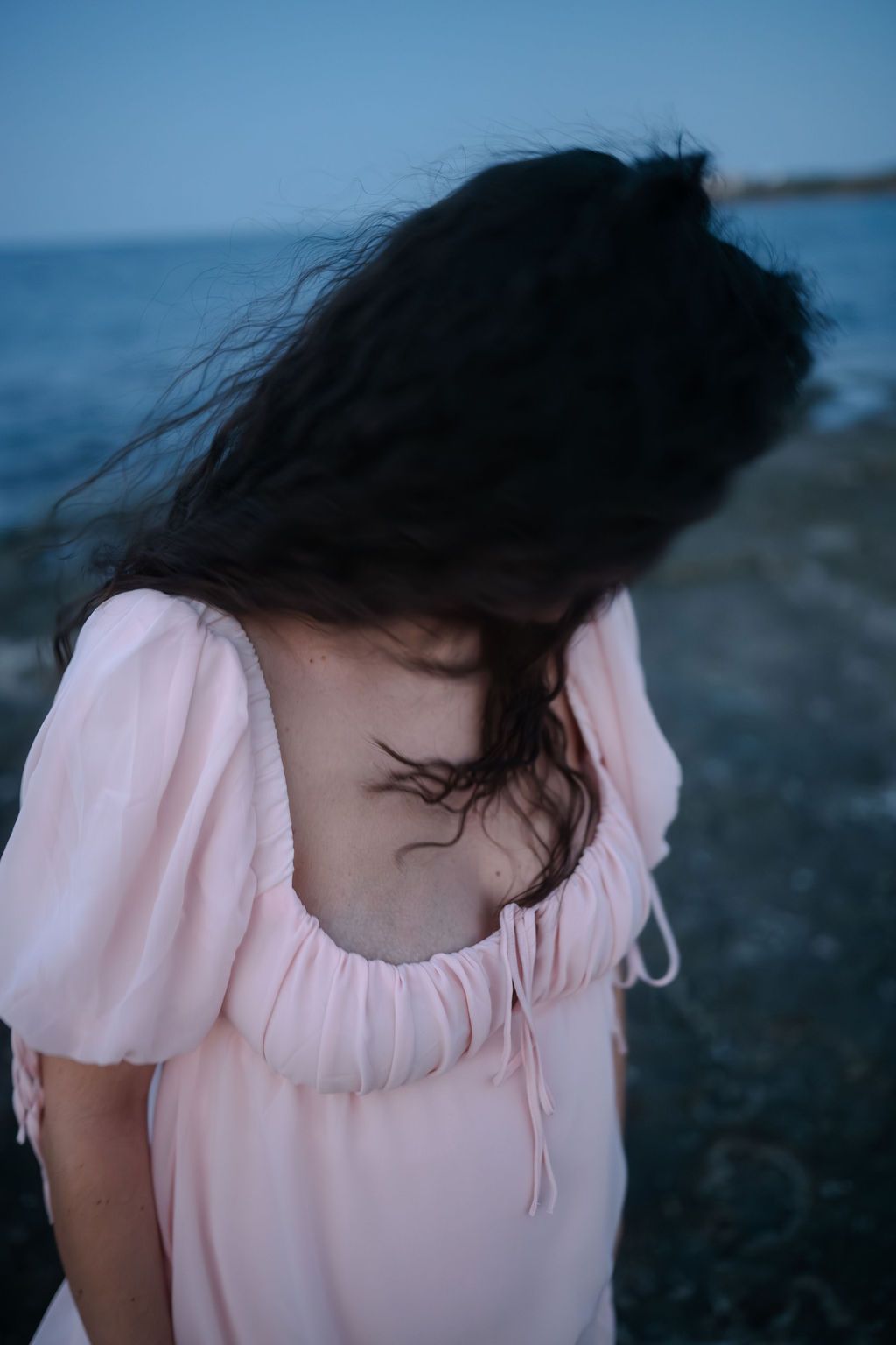 A sequence of photos showing dark hair blowing in the wind against a blue sky while wearing a pink blouse.