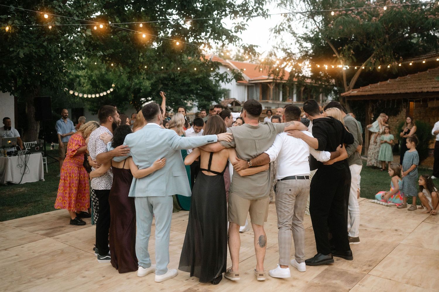 People dancing in a line at an outdoor evening event with string lights overhead.