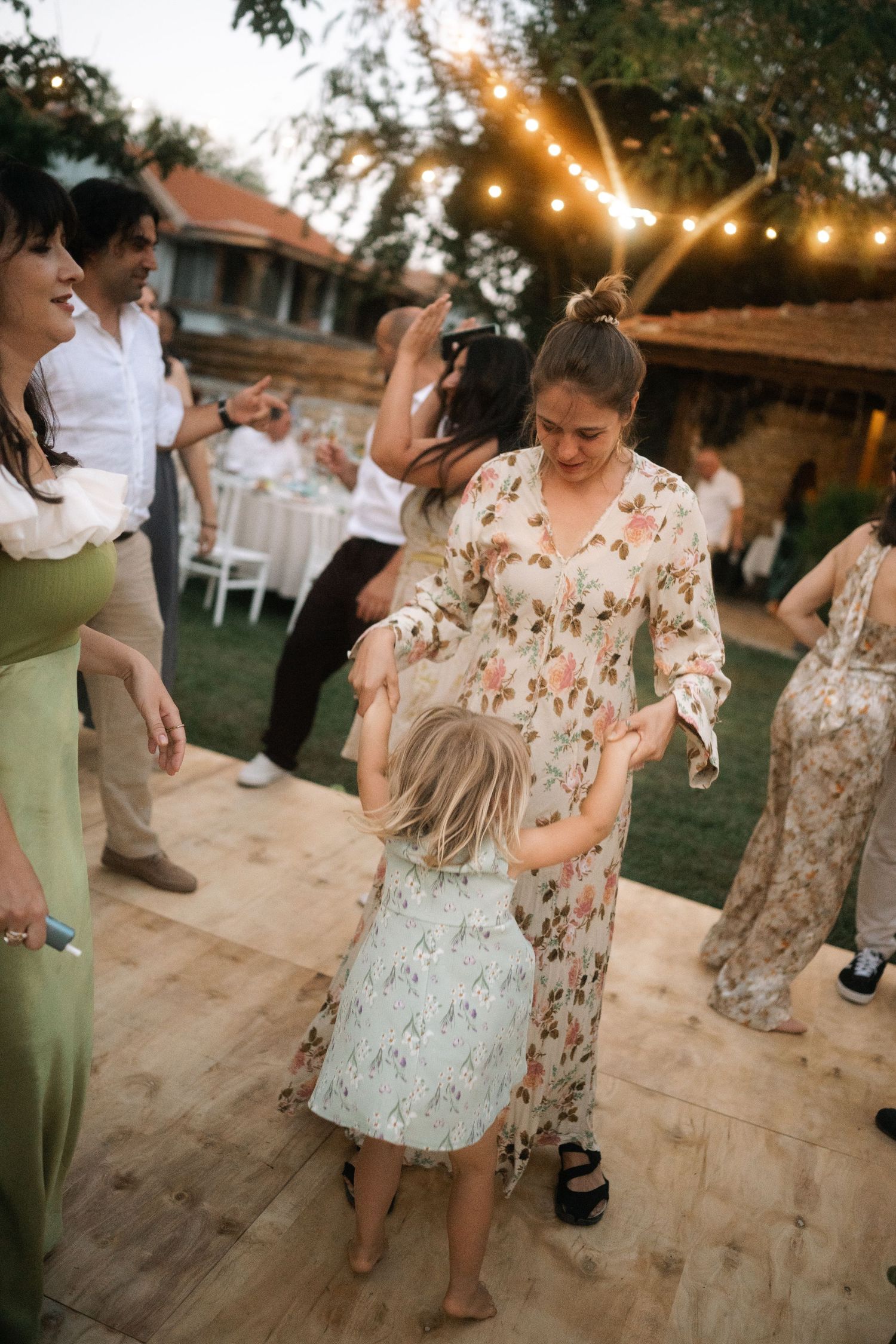 People dance on an outdoor patio during a festive celebration with string lights glowing overhead at dusk.