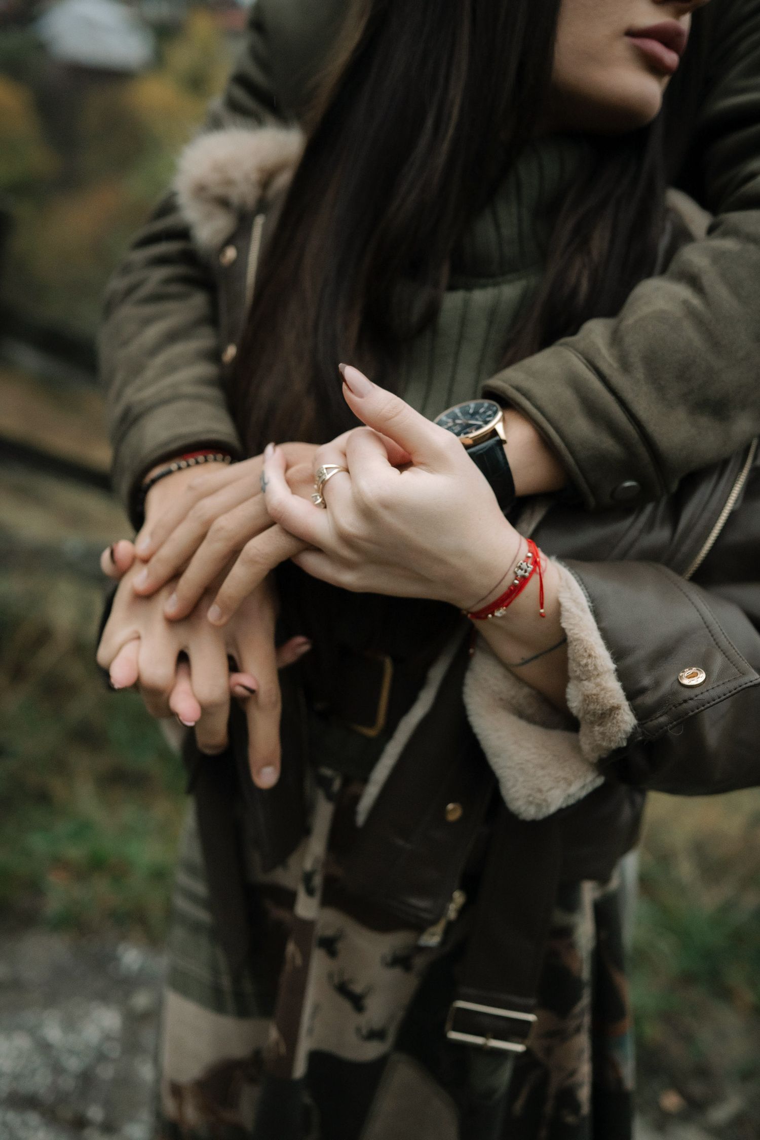 Close up of hands wearing winter coats showing an engagement ring with a red string bracelet.