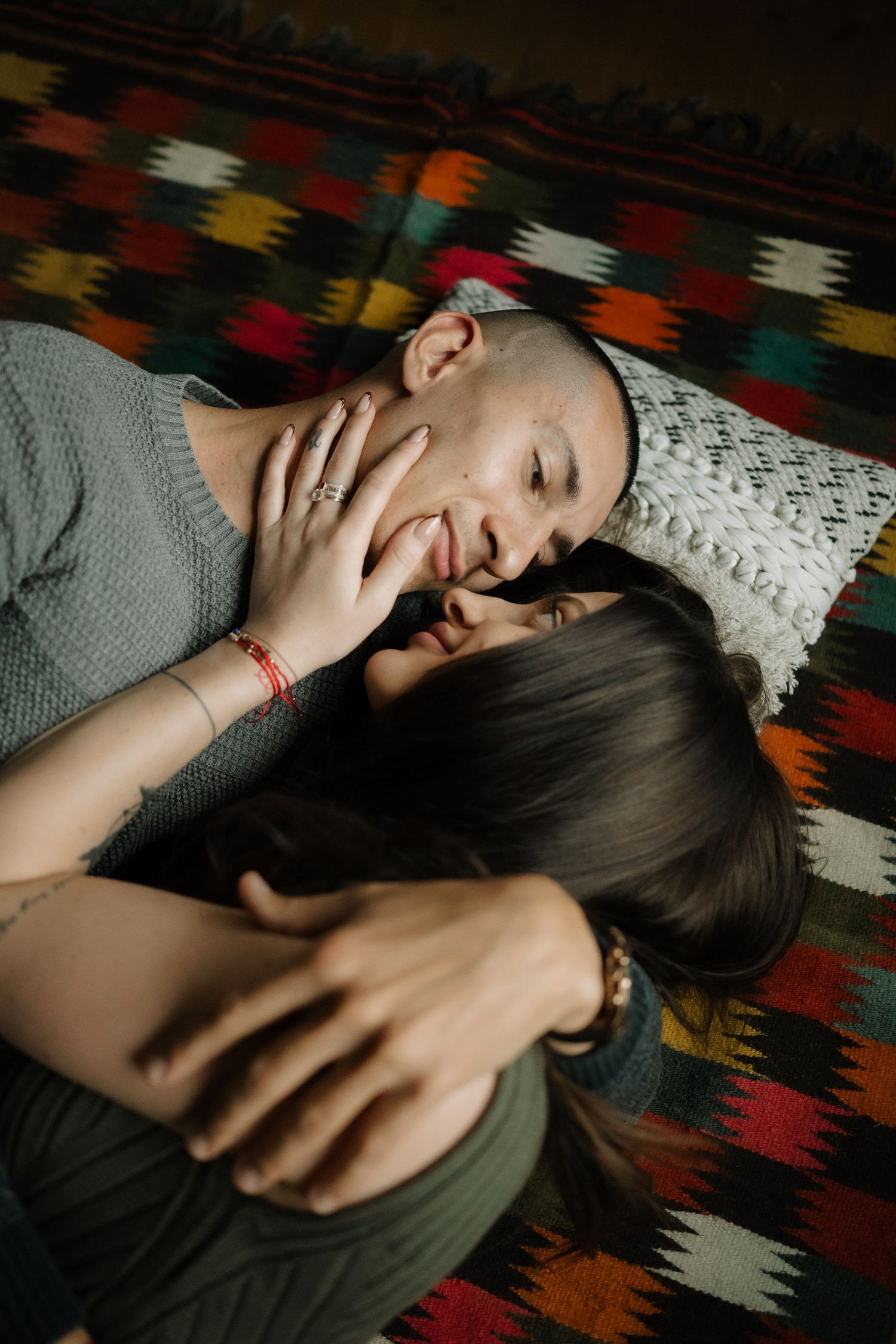 Person lying on colorful patterned rug expressing joy and laughter in casual indoor setting.