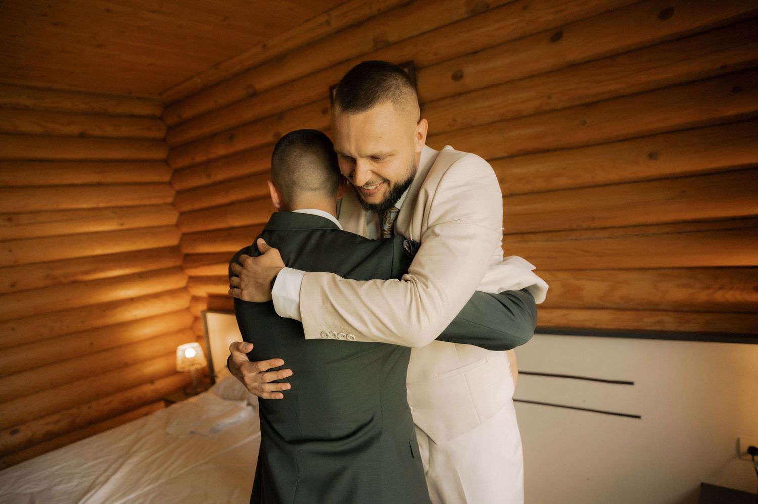 A person in a dark jacket receives a comforting embrace in a warm, wood-paneled room.