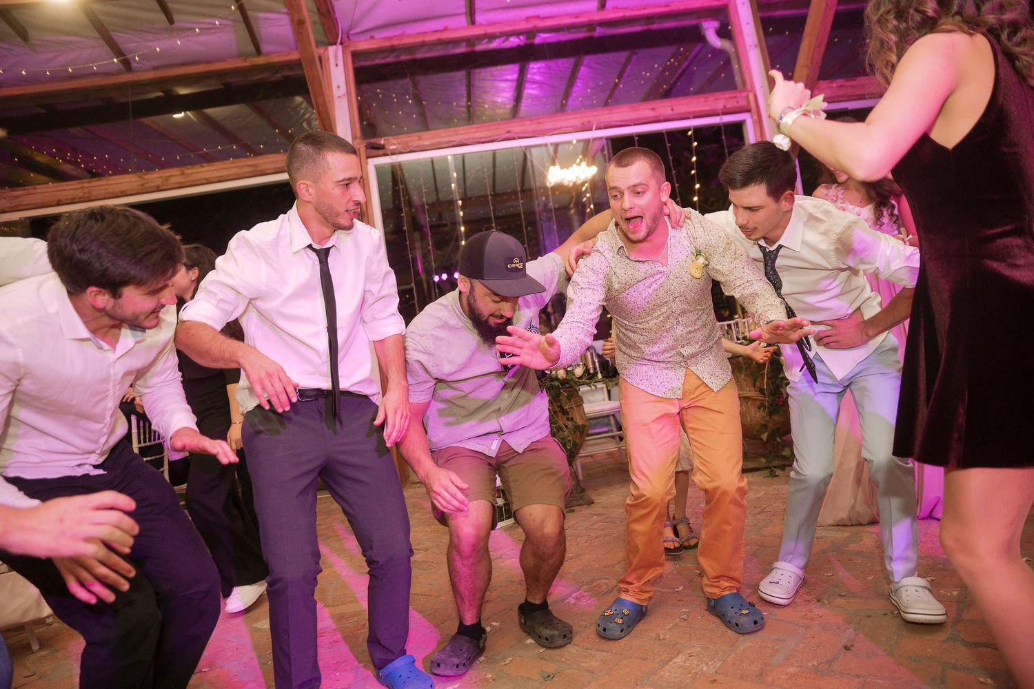 People dancing in a line on a dance floor illuminated by pink lighting at what appears to be a party or celebration.