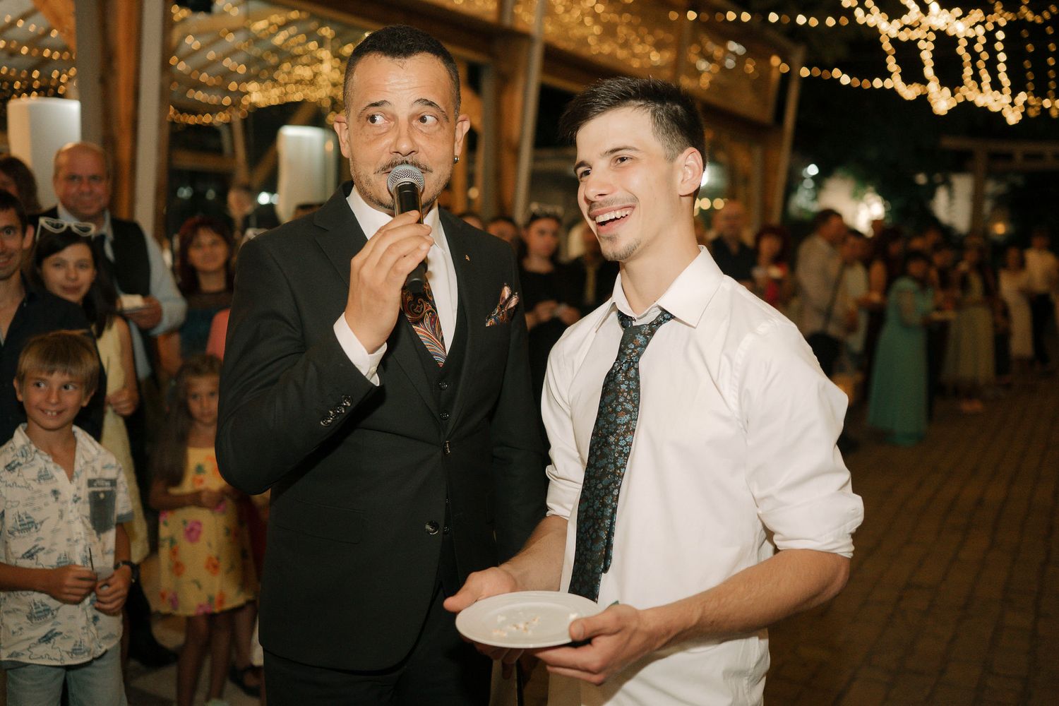 Wedding guests enjoying a lively reception party with string lights and festive atmosphere.