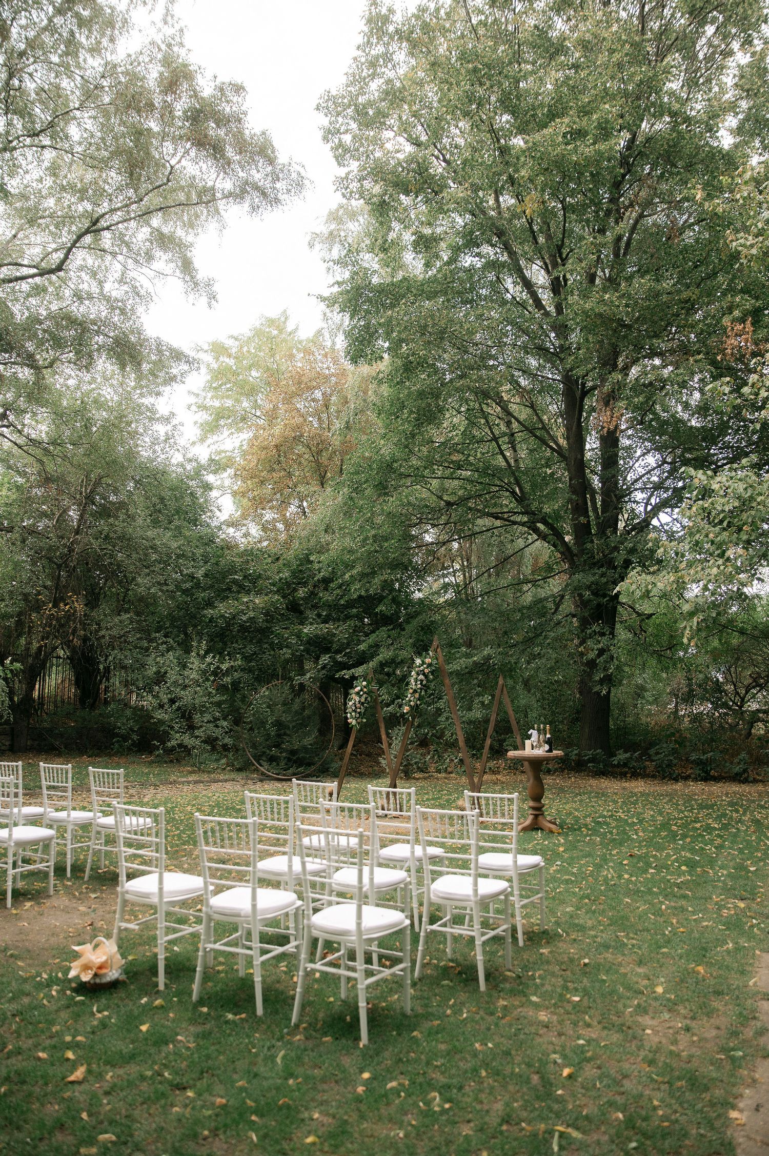 White wooden chairs arranged on a grassy lawn for an outdoor wedding ceremony with autumn trees in the background.