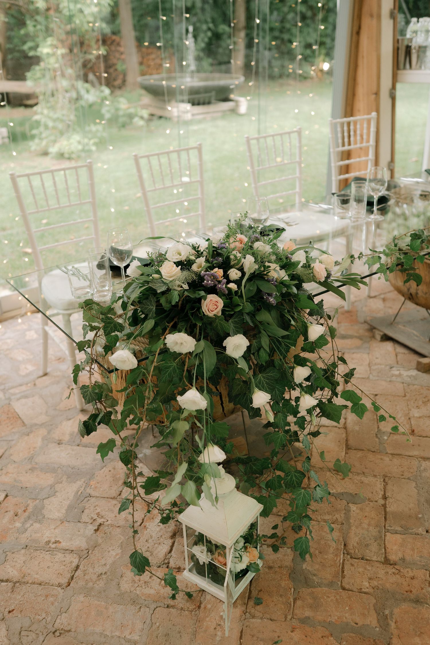 Elegant floral arrangements with white roses and greenery cascade down stone pillars at an outdoor wedding venue.