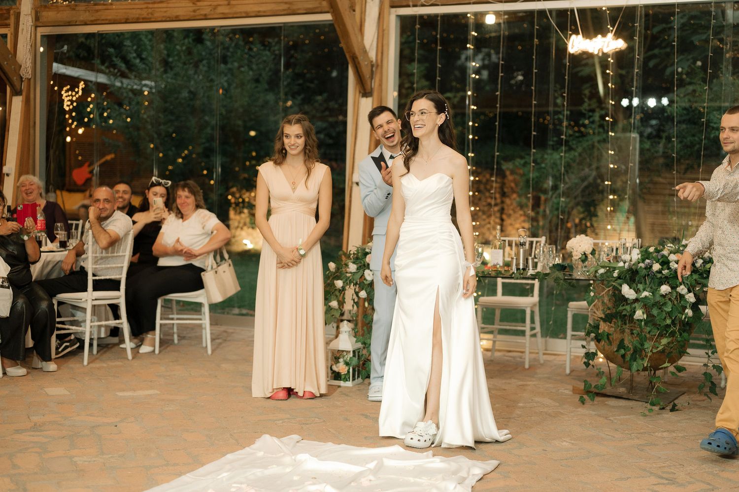 Wedding party members in light colored dresses dance together during an evening reception celebration.
