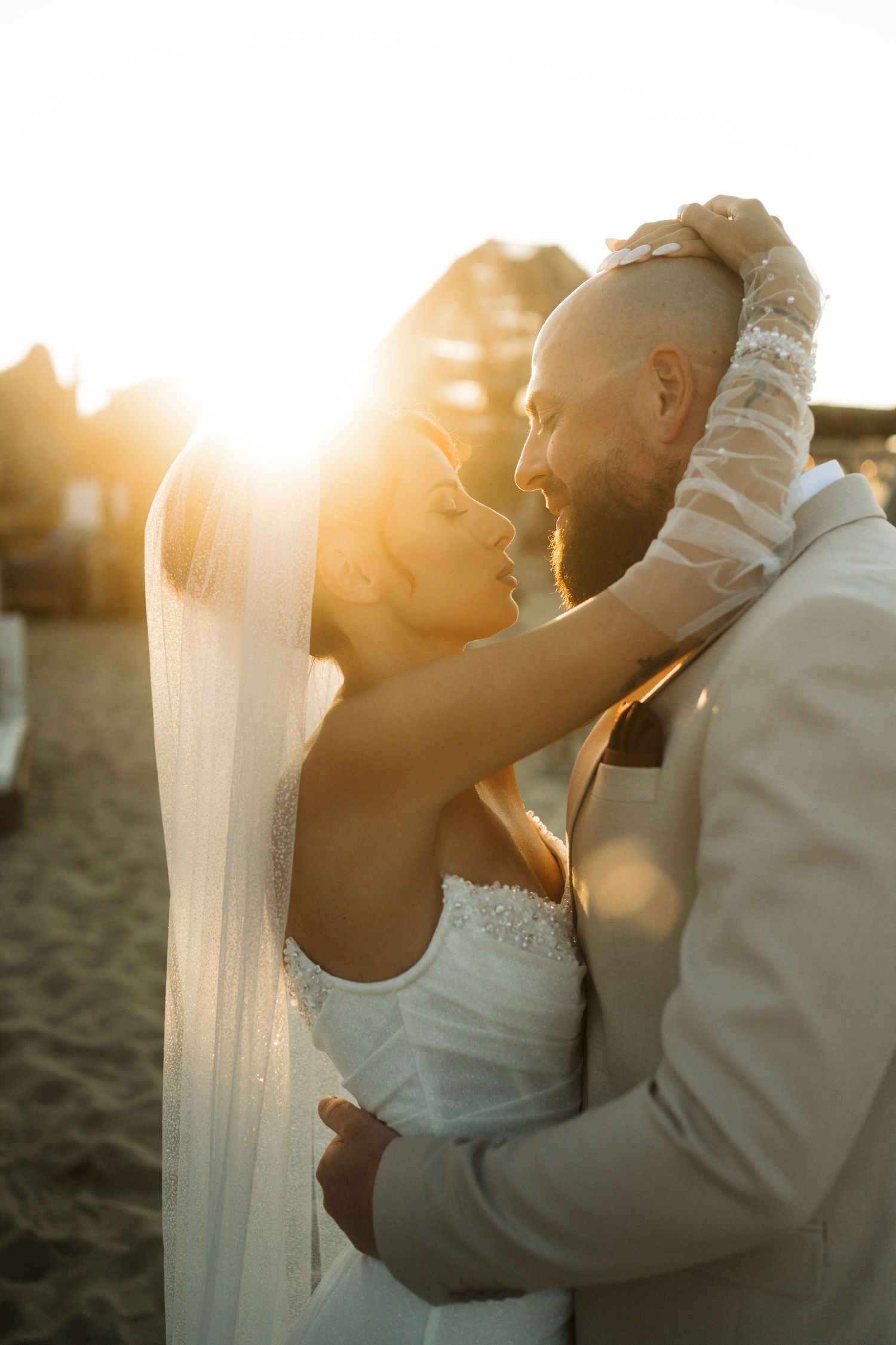 A romantic couple embraces on a beach at sunset with golden light filtering through their silhouettes.