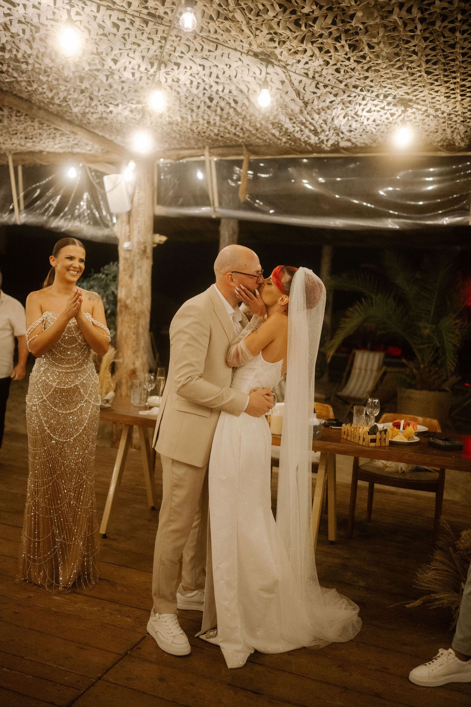 Wedding celebration on a rustic deck at night with string lights and guests in formal attire.