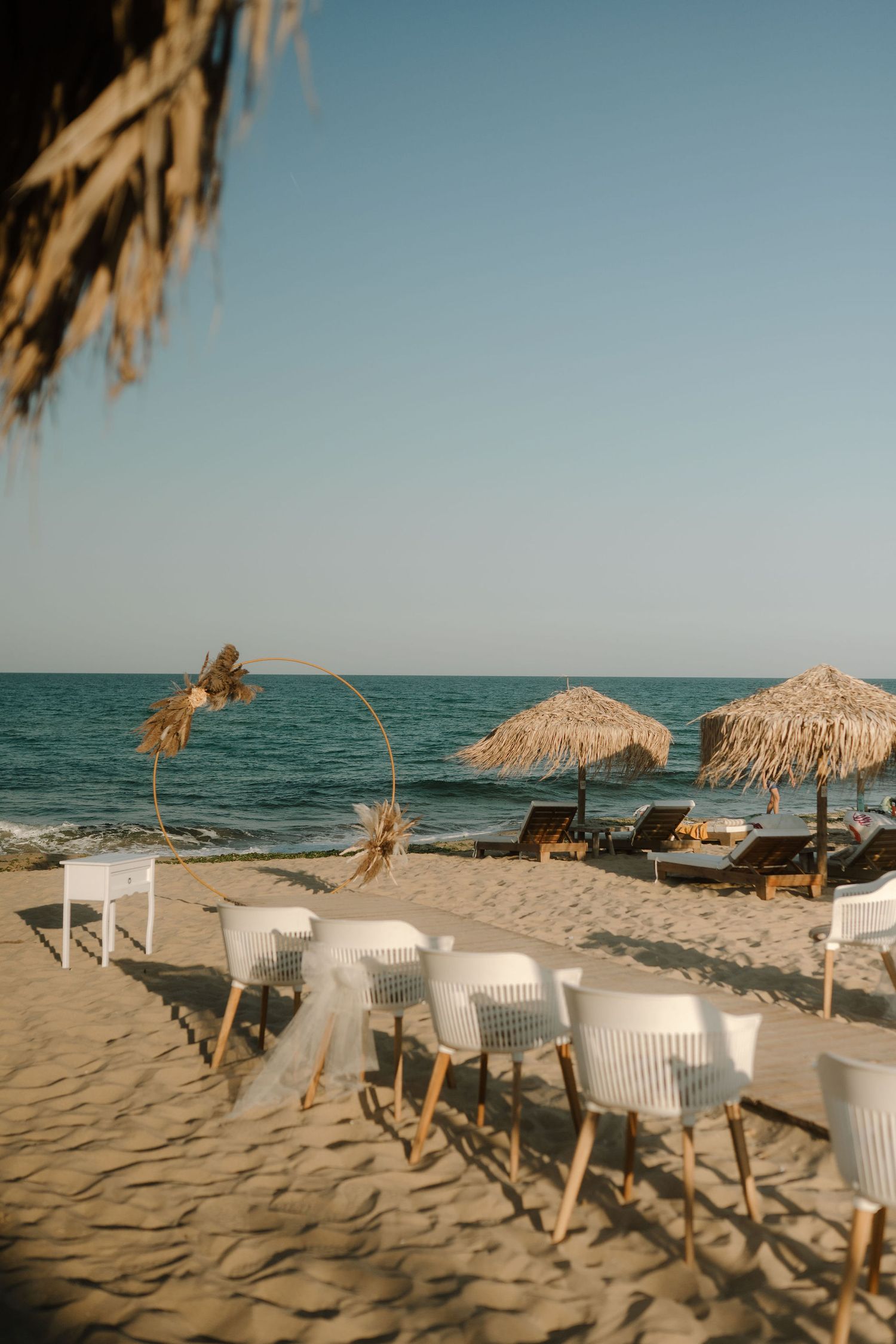 Beachfront lounge chairs and thatched umbrellas line a sandy shore with turquoise ocean waters in the background.