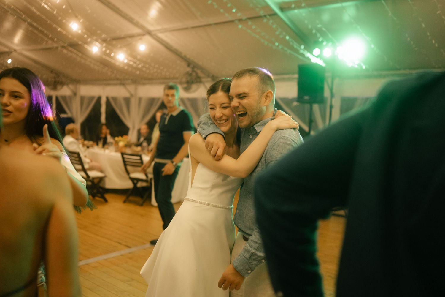 Colorful lights illuminate dancers on a wooden floor during an evening reception.