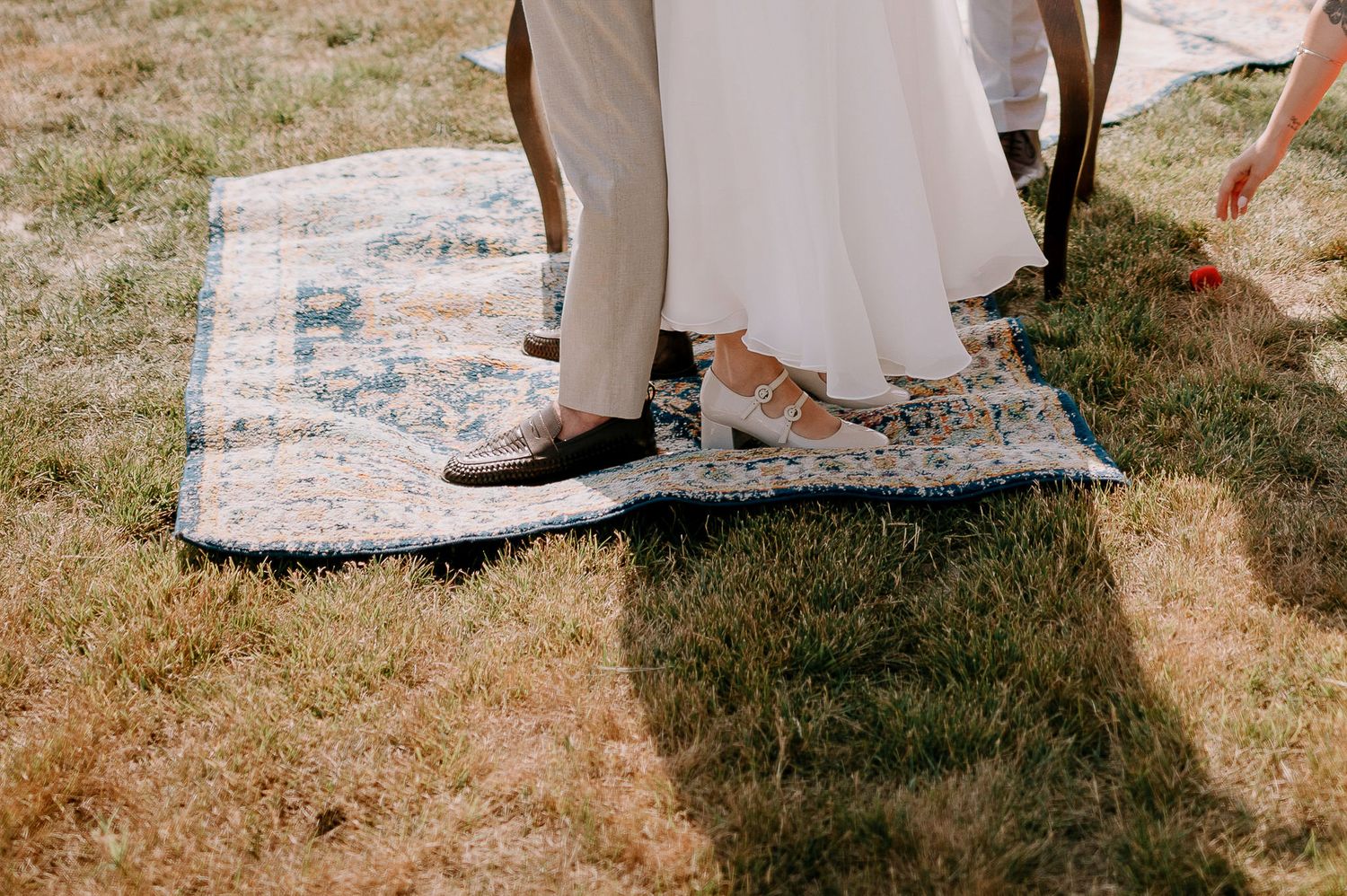 Wedding guests dance and celebrate on a decorative rug outdoors.
