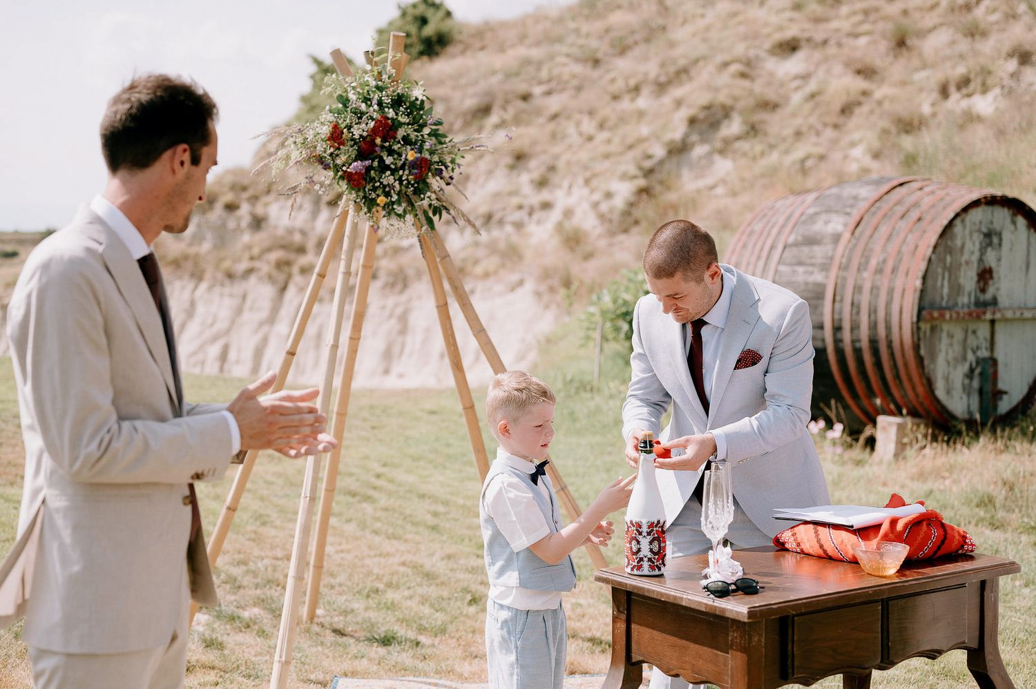 Wedding reception setup with rustic wooden furniture and decor on hillside vineyard.