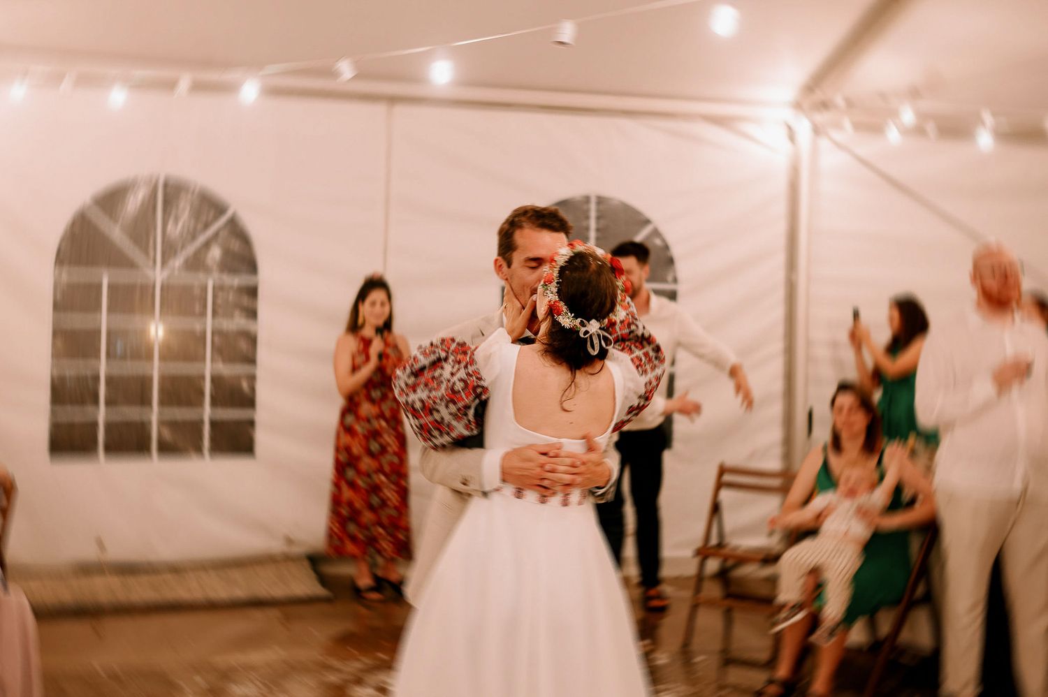 Wedding party enjoying festivities under string lights in an elegant tent setting.