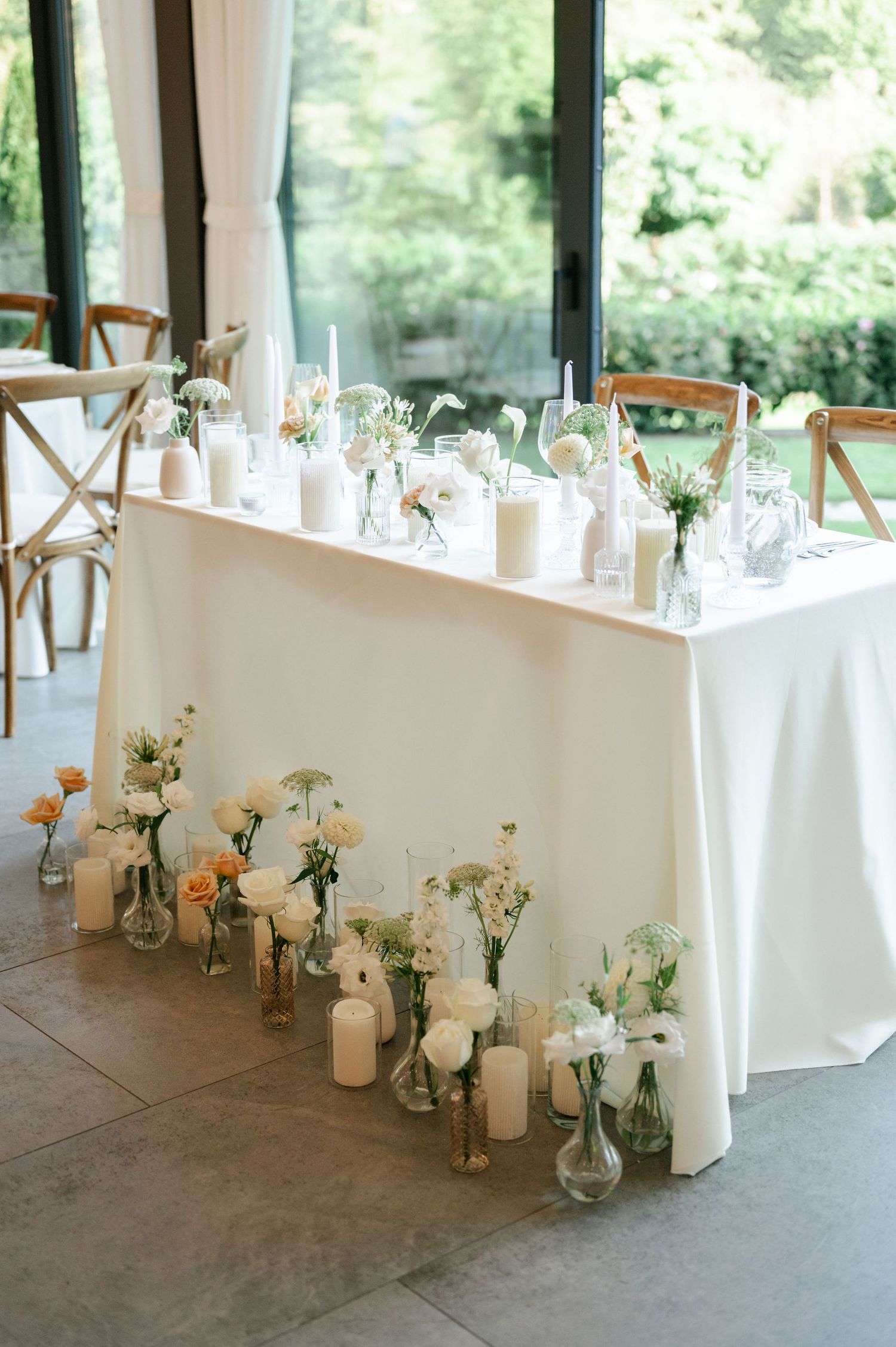 White-clothed table decorated with glass vases and candles arranged along floor level.