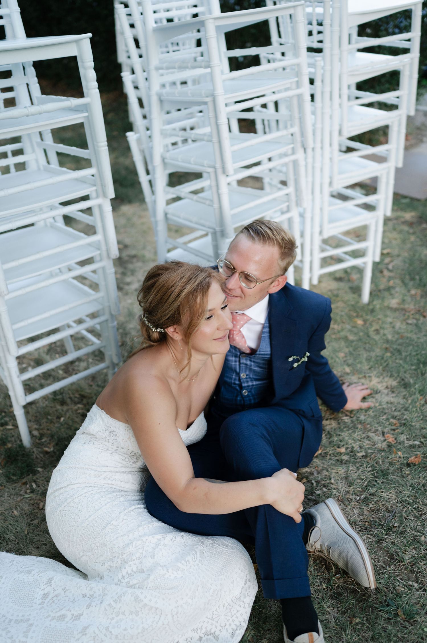 Candid wedding portrait captures couple's laughter during outdoor photo session near white chairs.