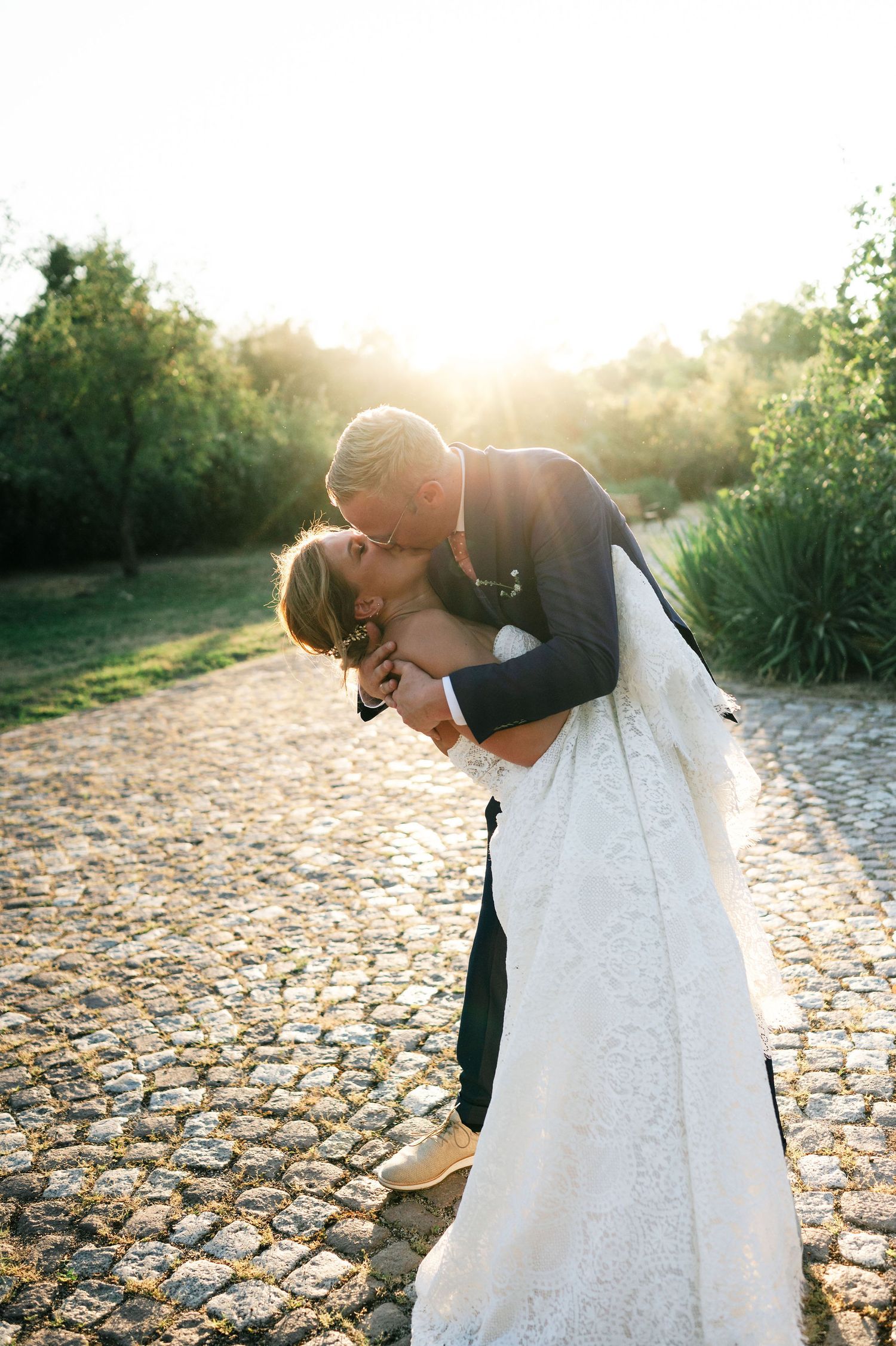 Newlyweds share an intimate kiss on a rustic stone path during golden hour.