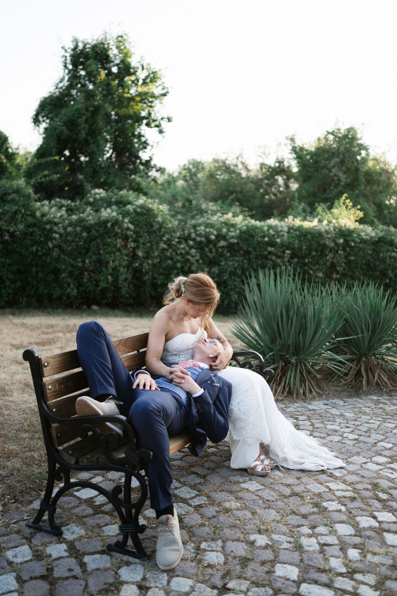 Wedding couple shares romantic moments on an outdoor bench surrounded by landscaped gardens.