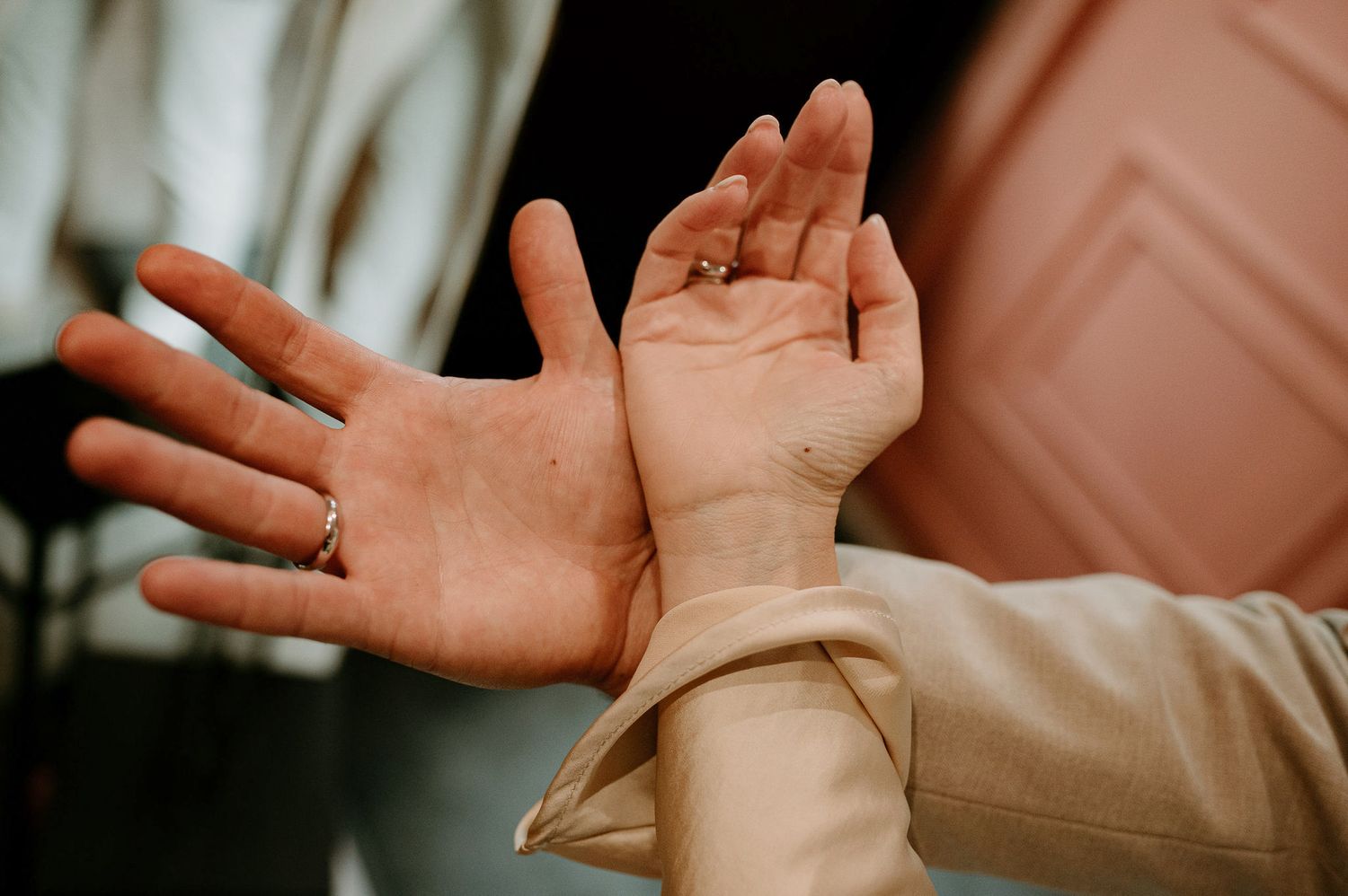 Close-up of hands making expressive gestures against a warm-toned background.