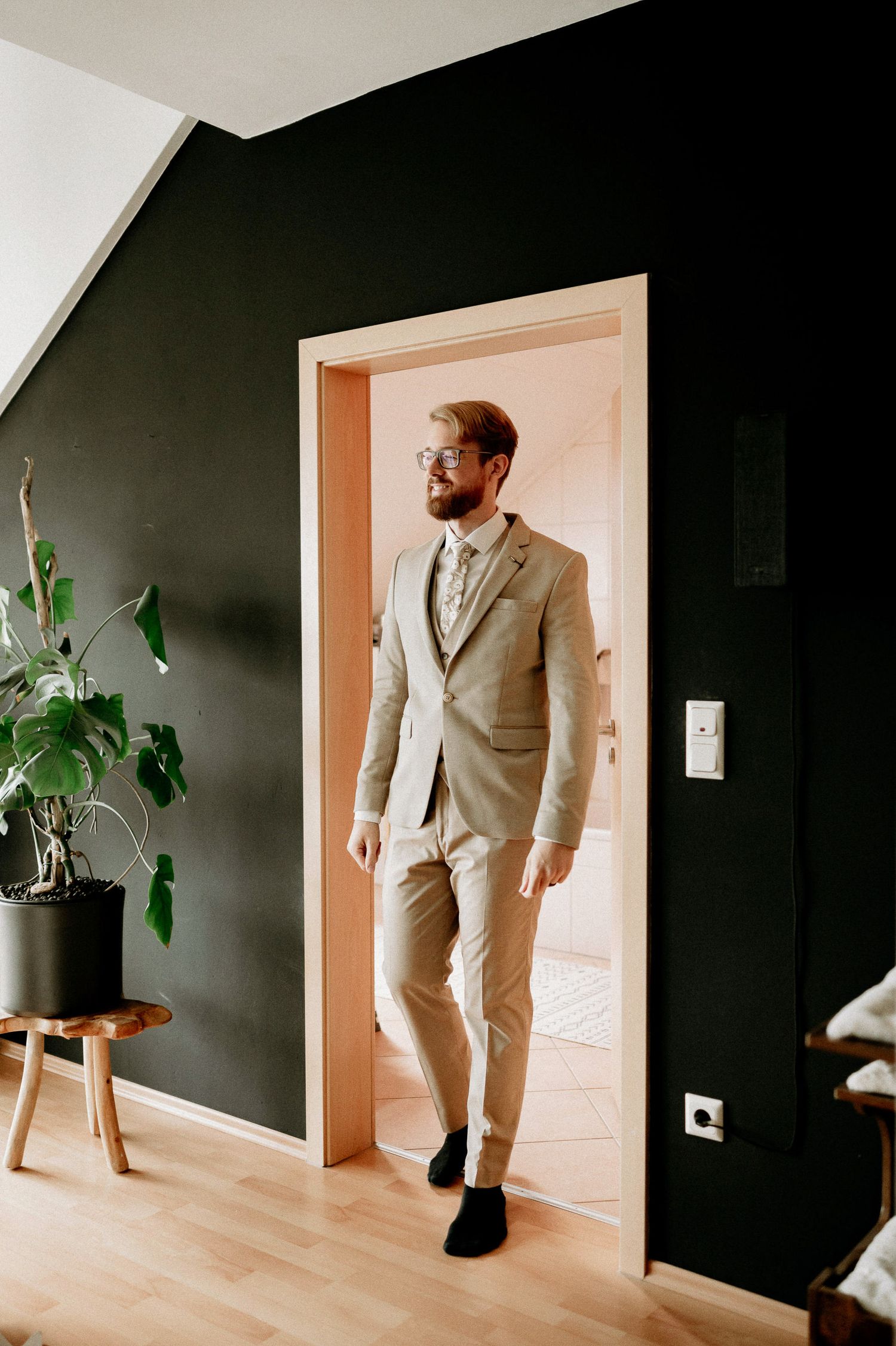 A modern room with black walls features someone wearing a beige suit standing in a doorway.