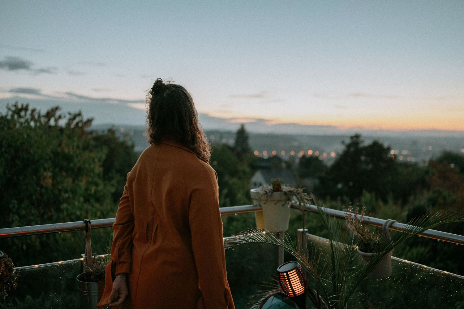 Person in brown jacket overlooking scenic sunset view from balcony.