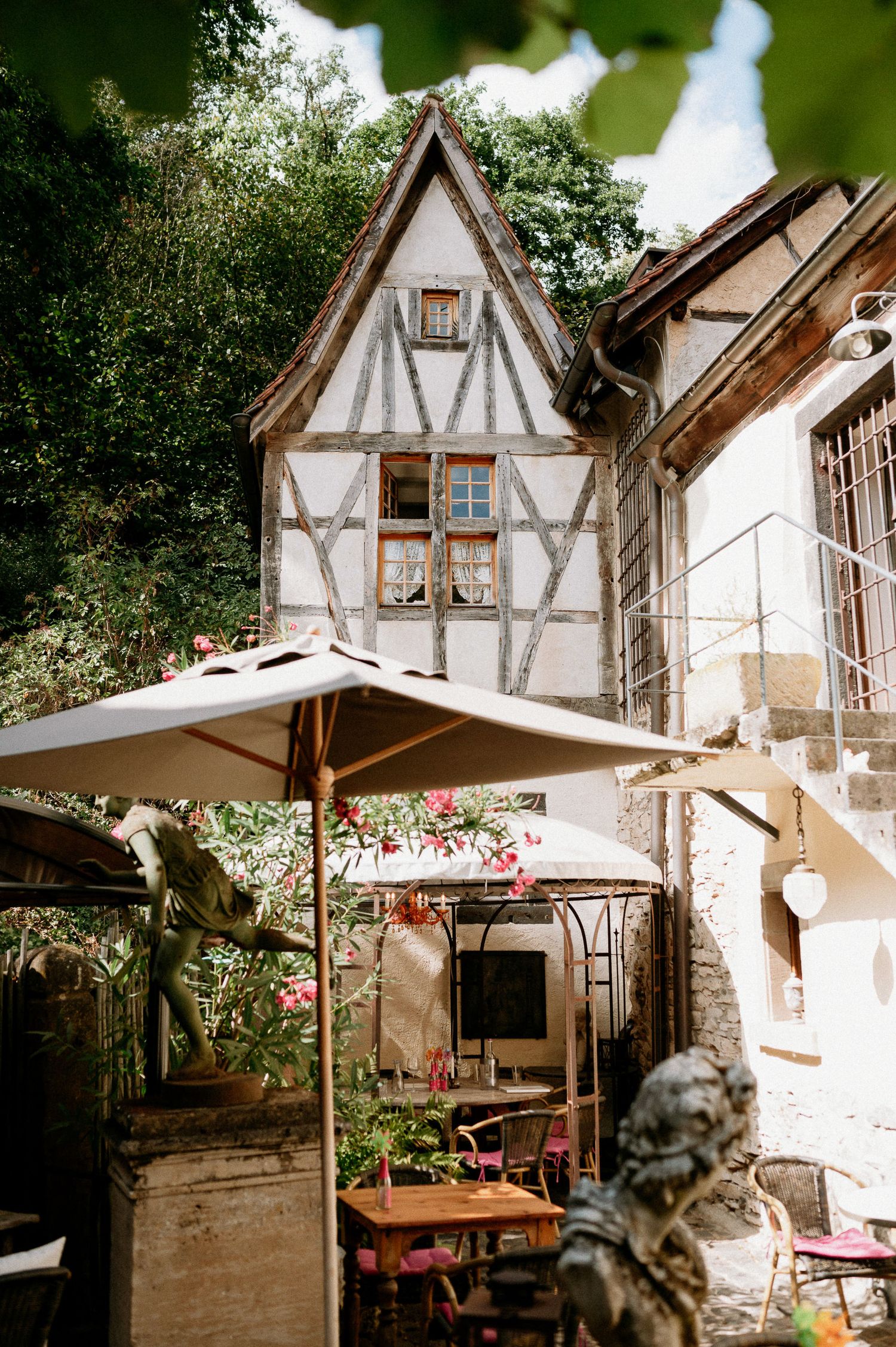 Rustic half-timbered cottage with white walls and exposed wooden beams surrounded by lush greenery.
