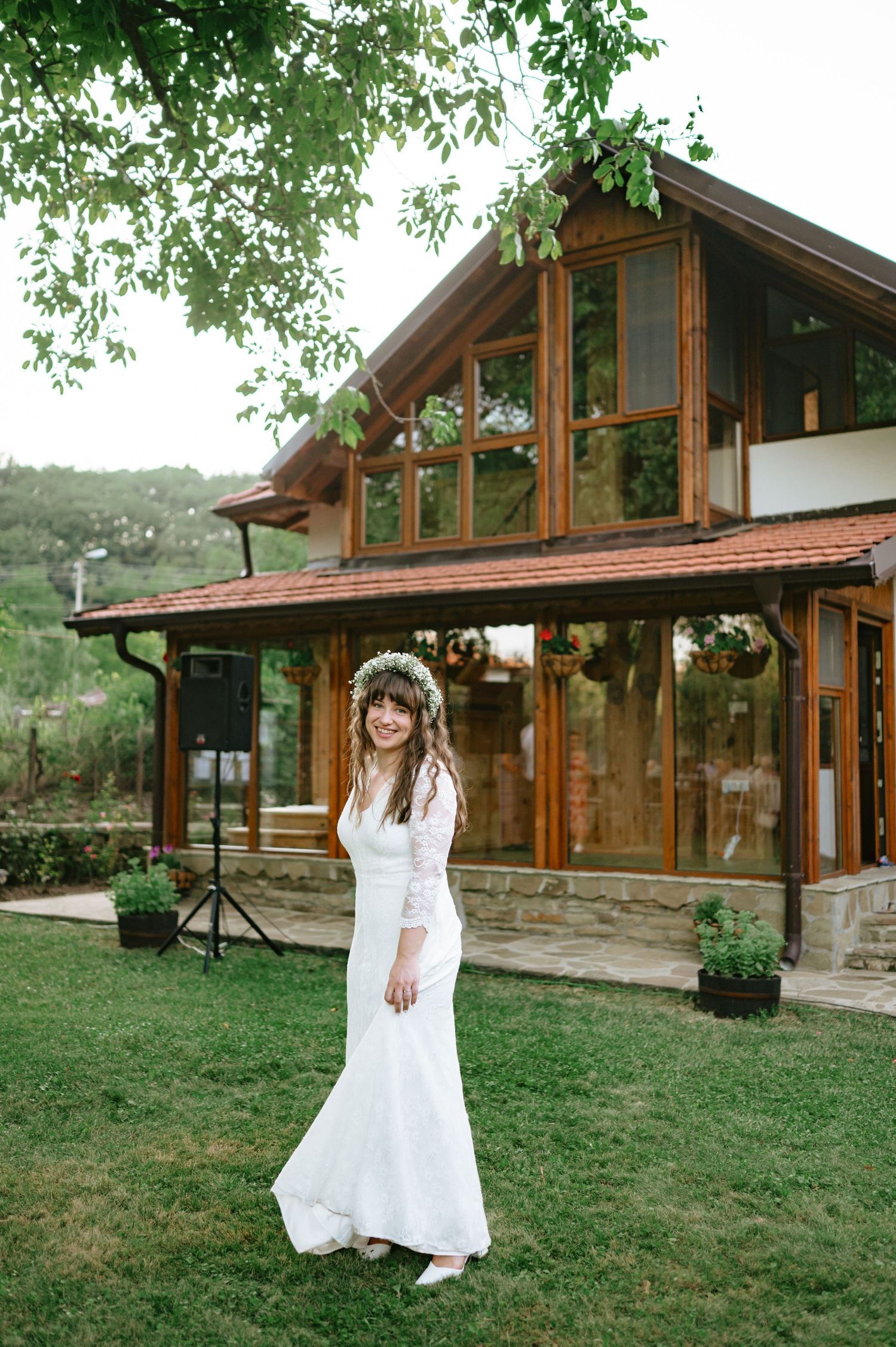 A bride in white dress twirls joyfully on grass in front of rustic cabin.
