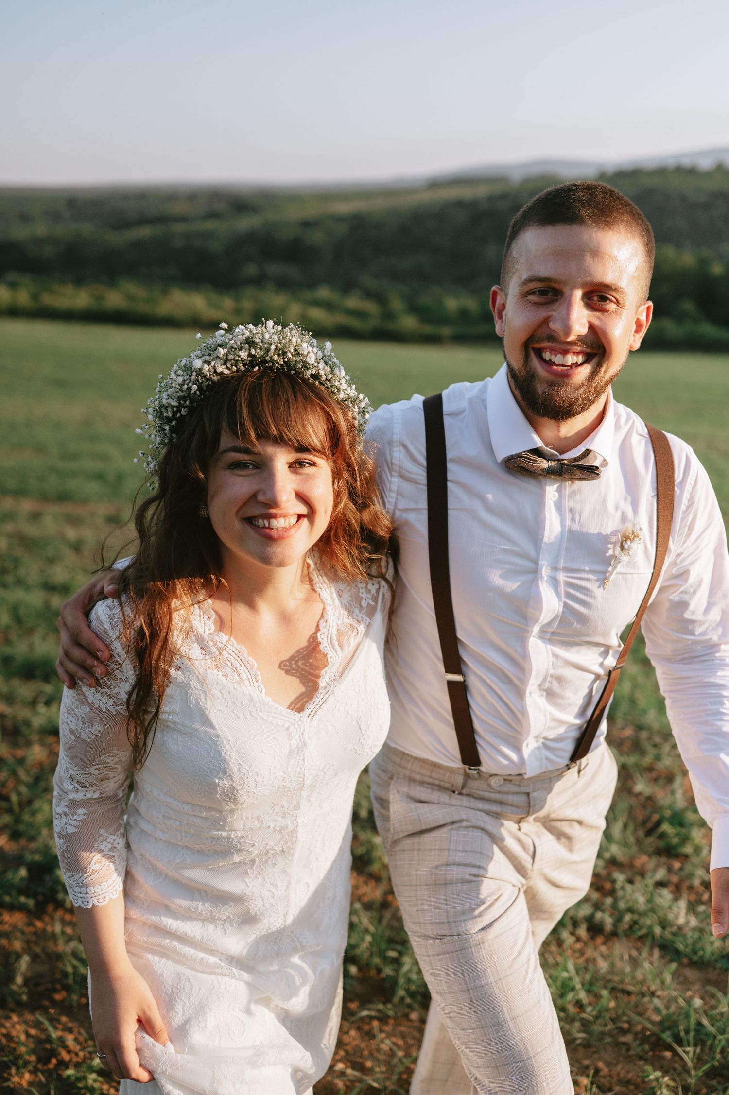 A romantic wedding photoshoot in a field at golden hour with a couple in white and rustic attire.