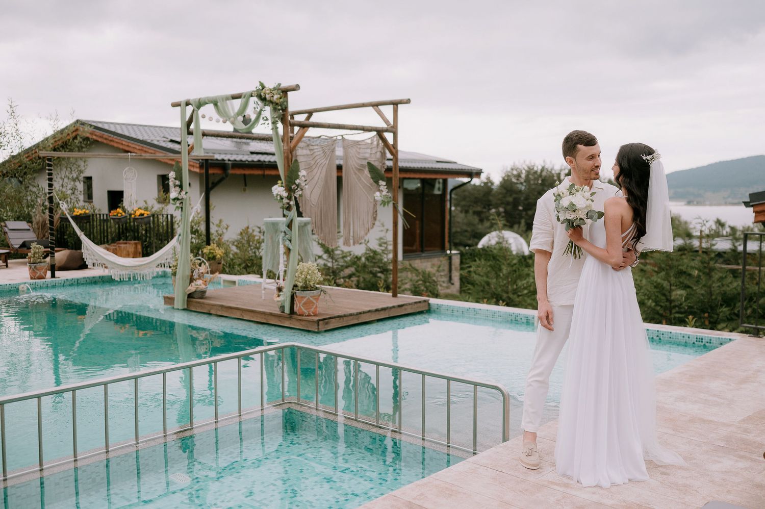 Outdoor wedding ceremony space with wooden arch and floral decorations beside a pool.