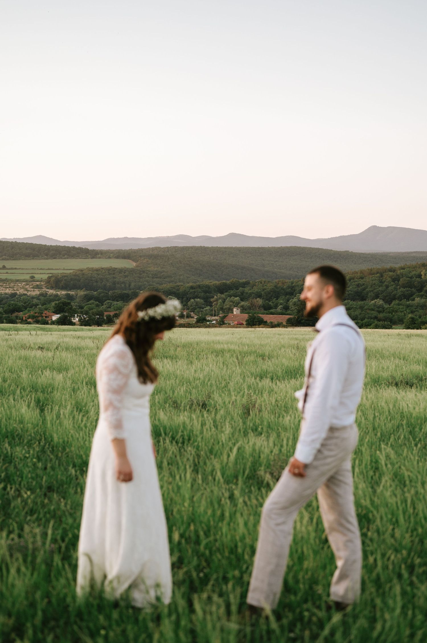 A couple in white outfits walks through a scenic mountain meadow at sunset.