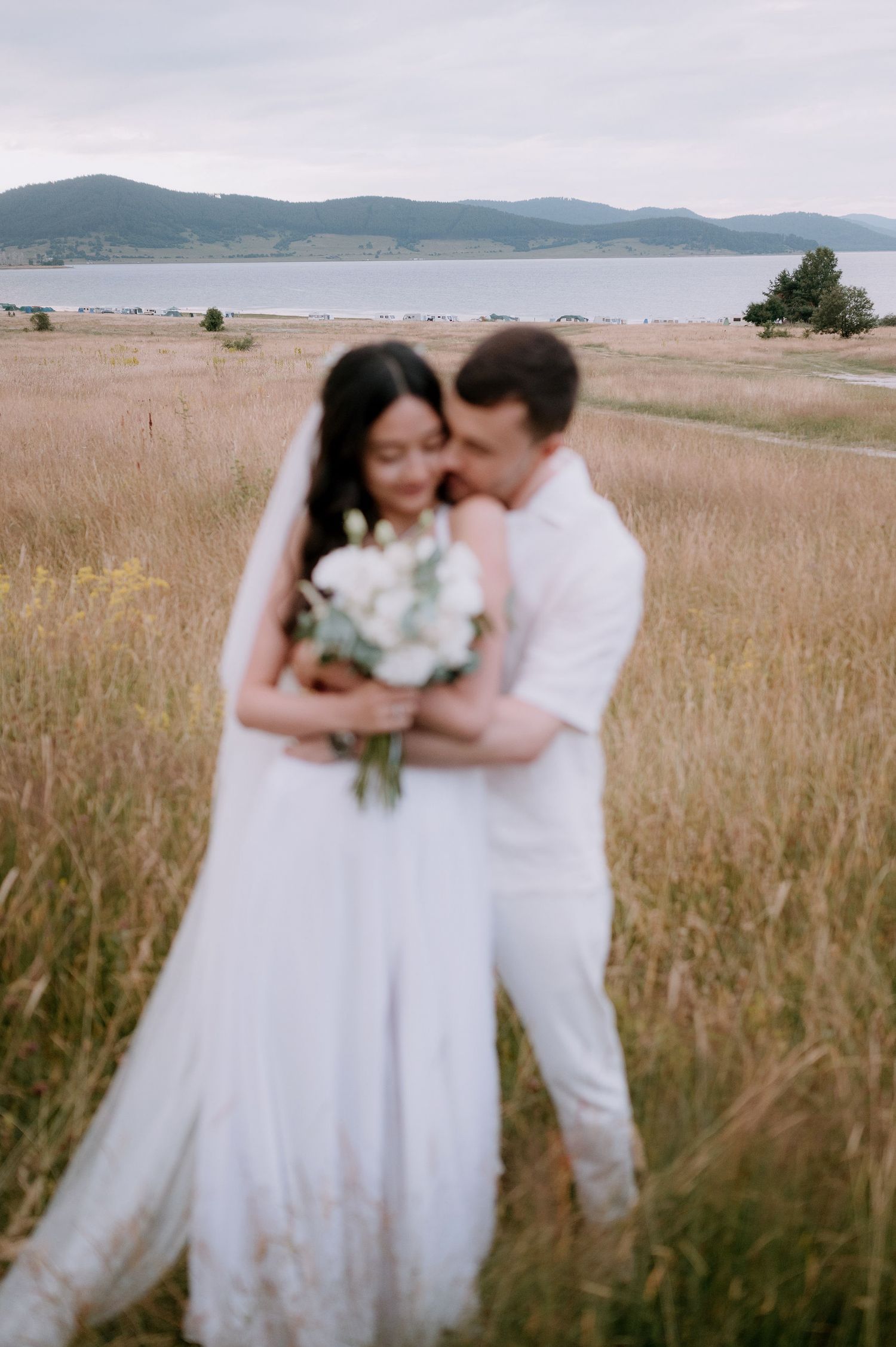 Wedding couple shares intimate moments in a golden field with water views.