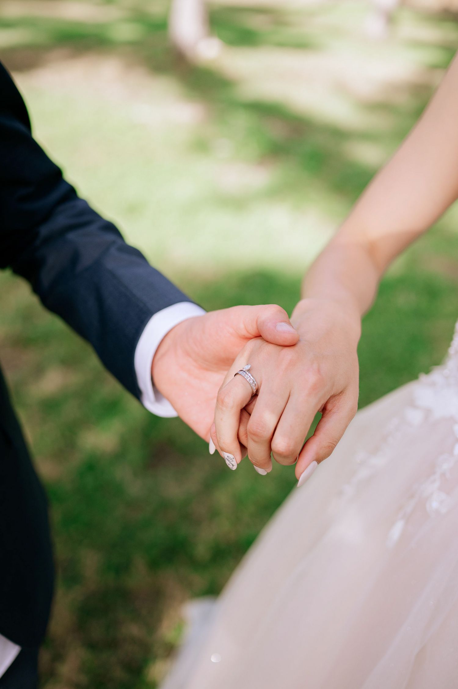 Close-up details of hands with wedding rings against white dress fabric outdoors.