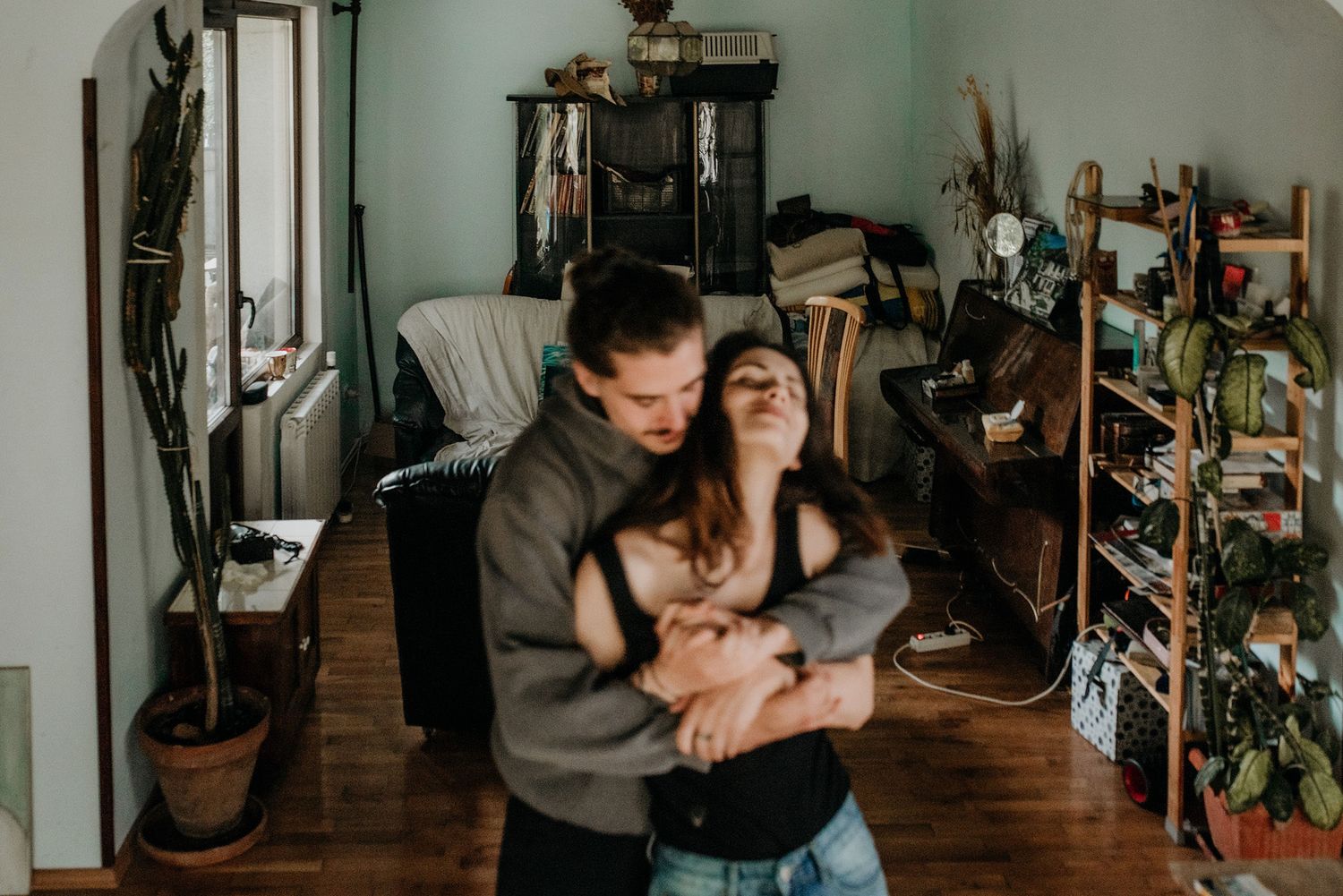 A couple embraces intimately in their living room with houseplants and decor visible in the background.