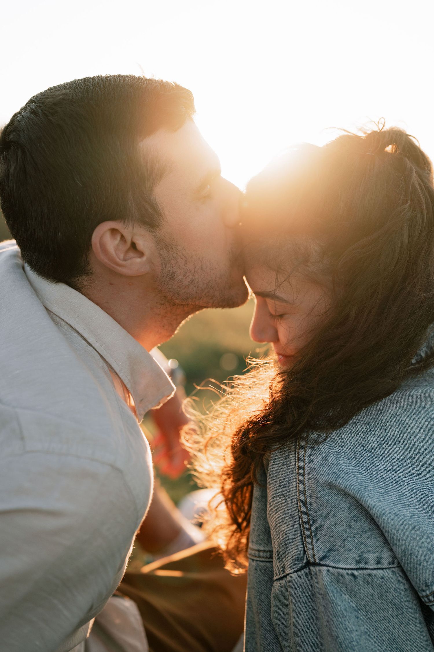 A romantic couple shares an intimate moment in golden sunlight, with her wearing denim and him in white.
