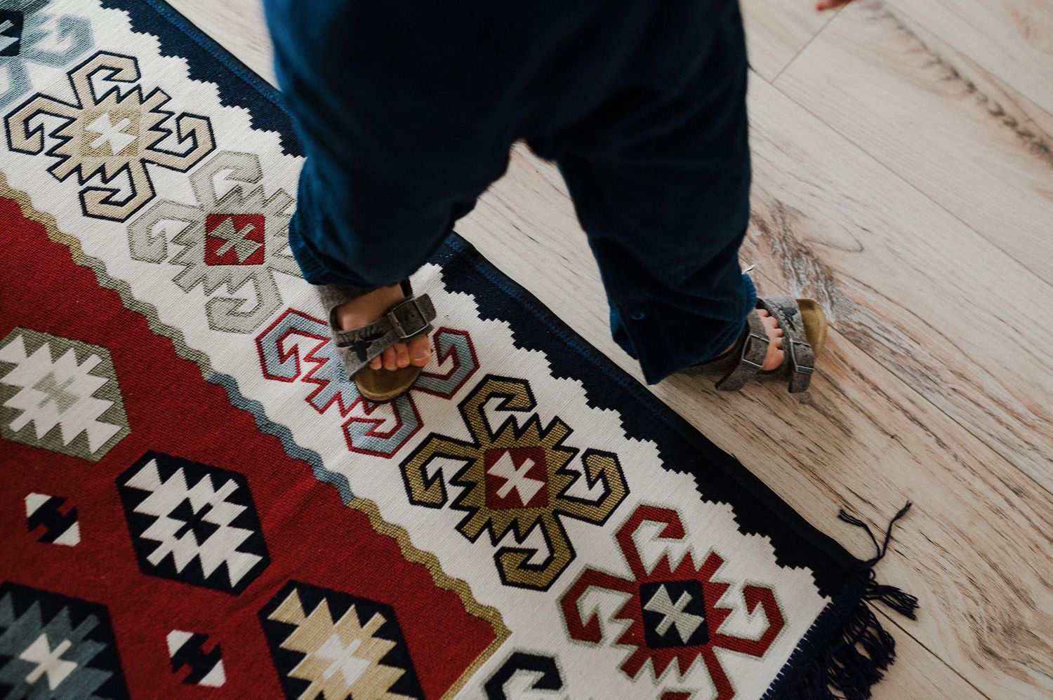 Close-up view of feet standing on a colorful patterned rug with geometric designs in red and white.