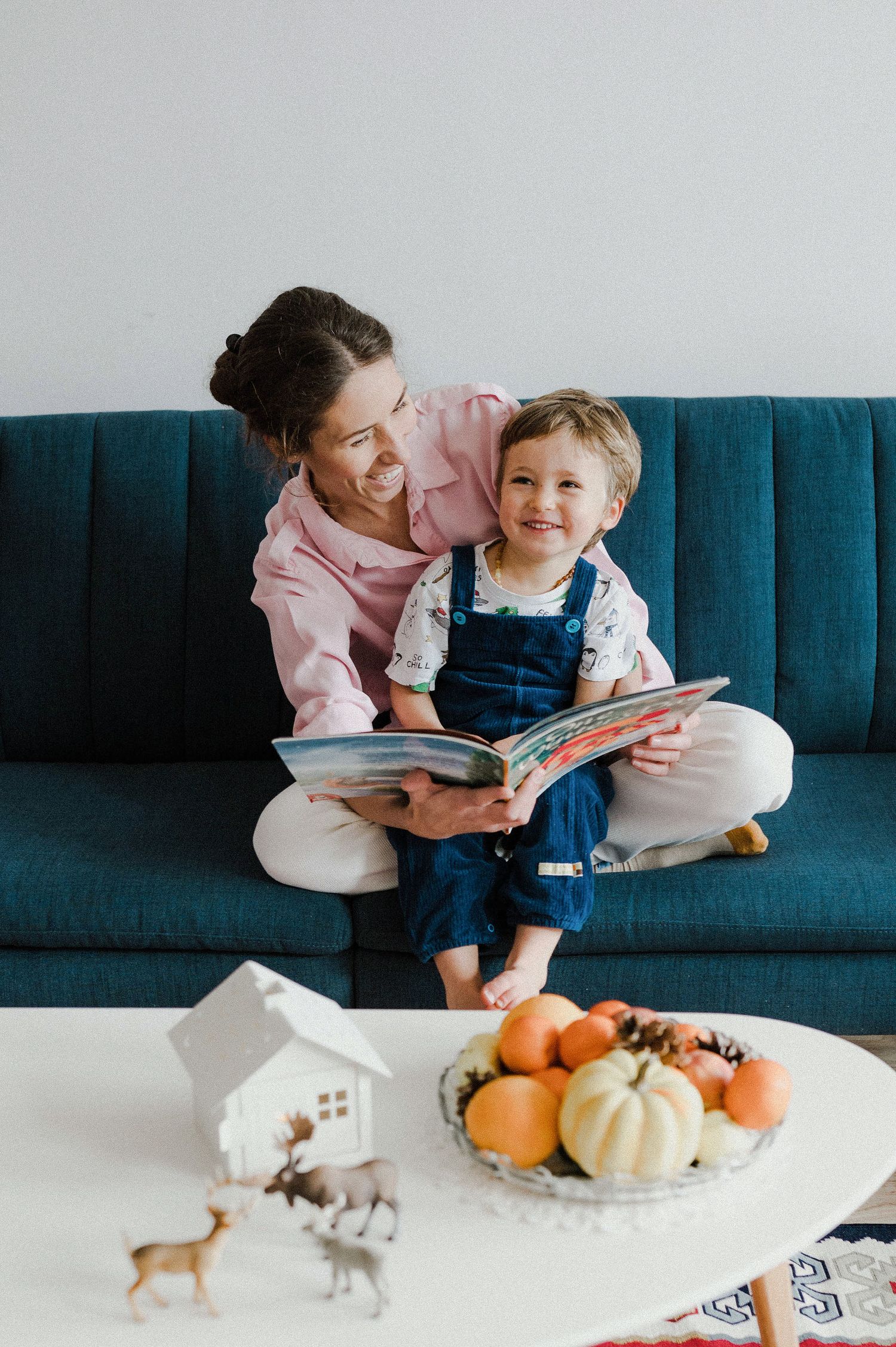 Parent and child reading together on a blue couch with pumpkins and decorative items on the coffee table.