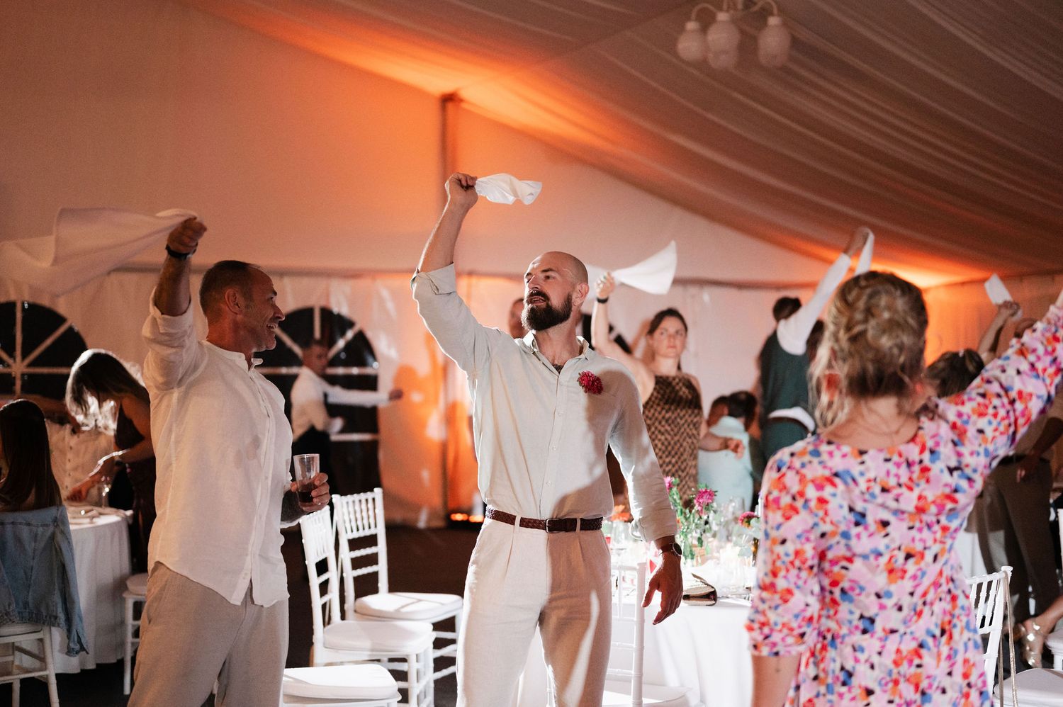 Wedding guests dance and celebrate on a tented dance floor decorated with red and pink floral patterns.