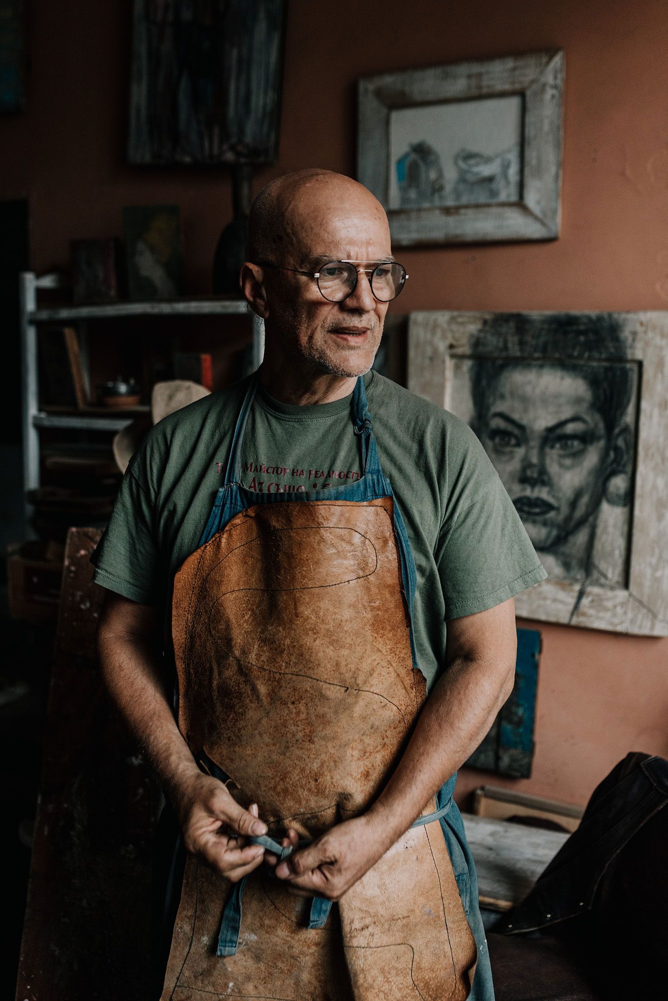Artist wearing a green shirt and well-worn leather apron in their creative studio space.