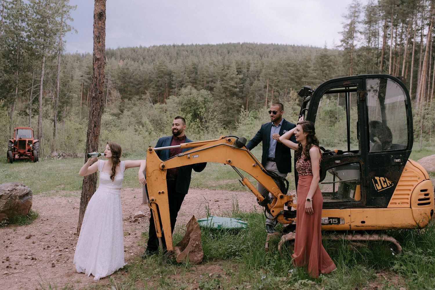 Wedding party poses near construction equipment in a rustic forest setting.