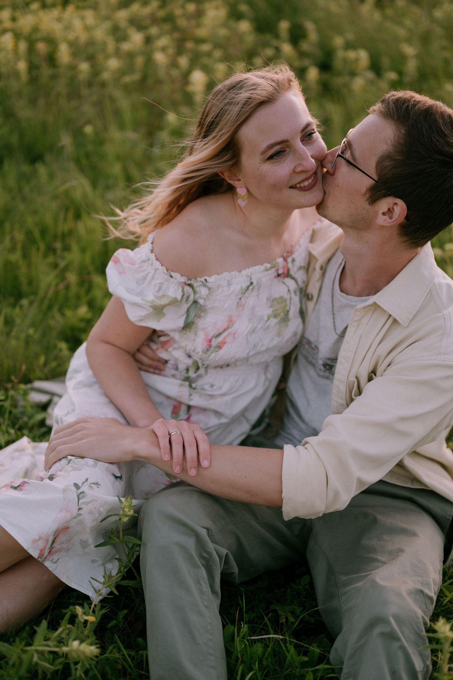 Joyful couple sharing intimate moment in field of yellow flowers during sunset.