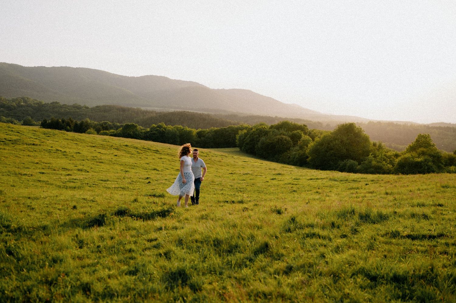 Couple exploring a scenic hillside meadow during golden hour.