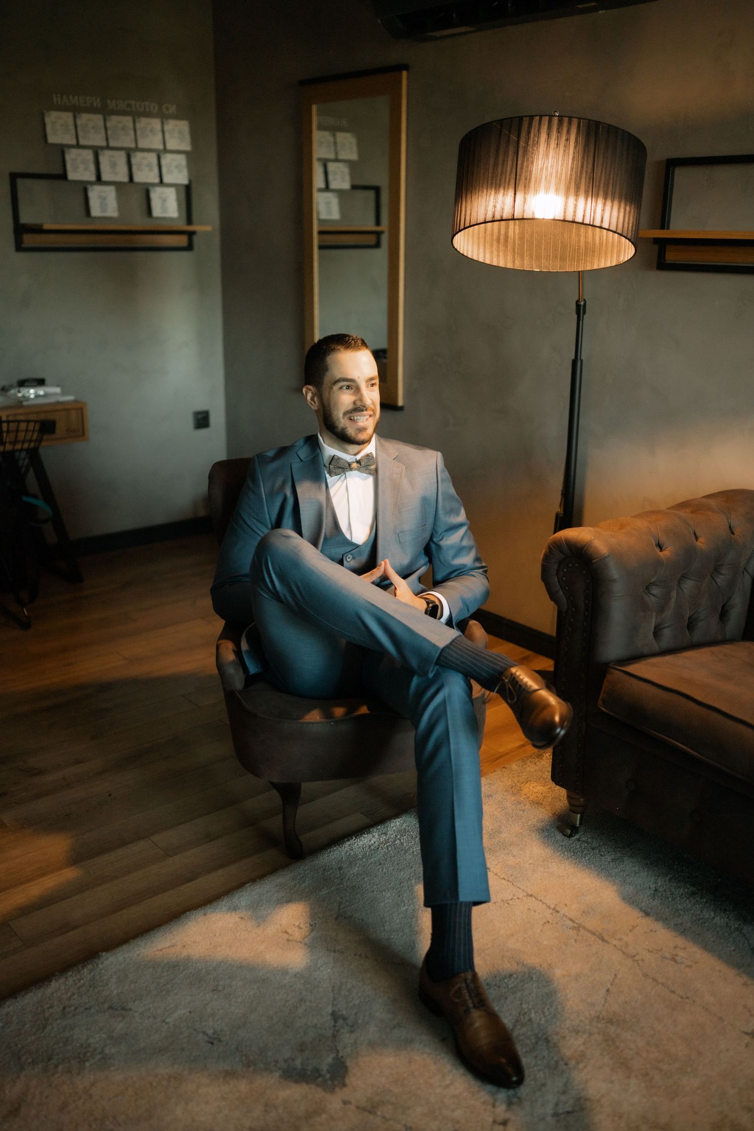 A person in a blue suit sits on a brown leather couch in a dimly lit room with modern decor.
