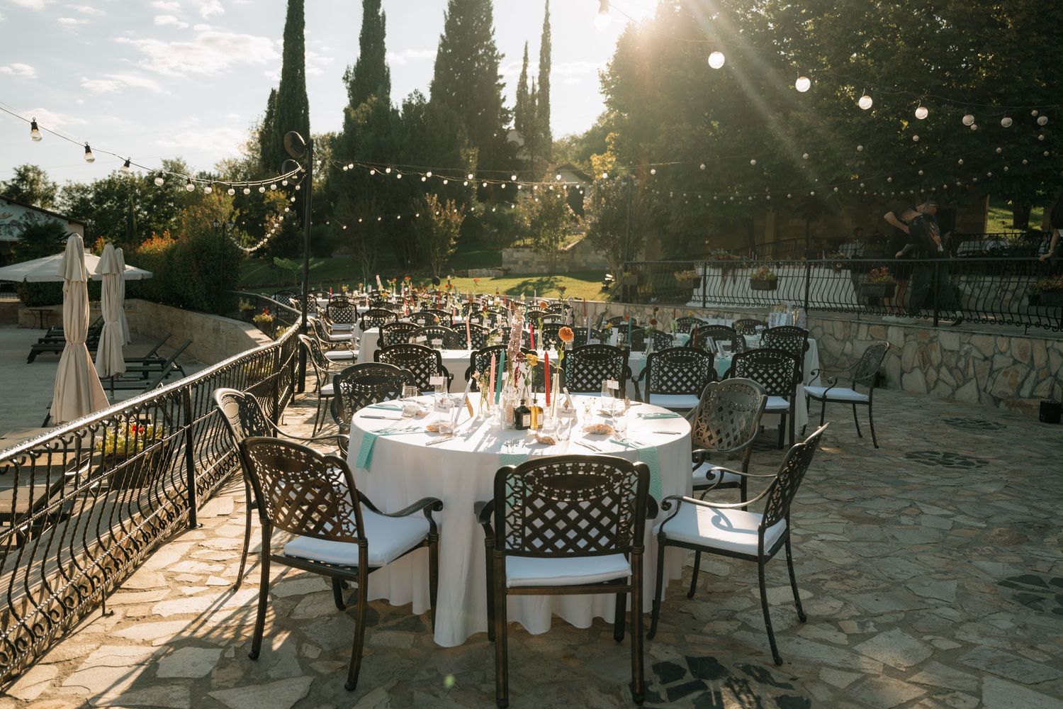 Elegant outdoor wedding reception venue at sunset with cypress trees and tables set for dining under golden light.